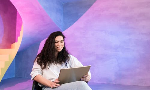 Frau sitzt mit einem Tablet auf dem schoß in einem pink-blau beleuchteten Raum Frau sitzt mit einem Tablet auf dem schoß in einem pink-blau beleuchteten Raum