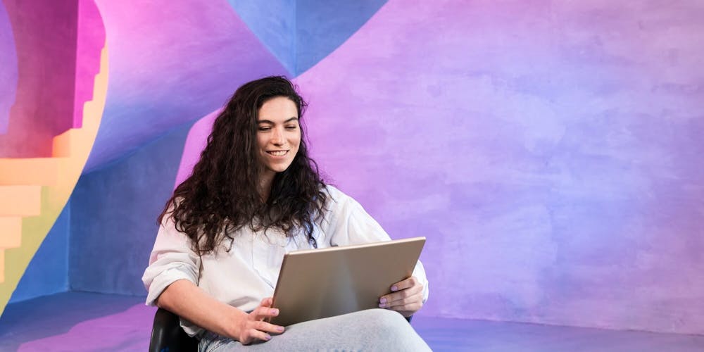 Frau sitzt mit einem Tablet auf dem schoß in einem pink-blau beleuchteten Raum Frau sitzt mit einem Tablet auf dem schoß in einem pink-blau beleuchteten Raum