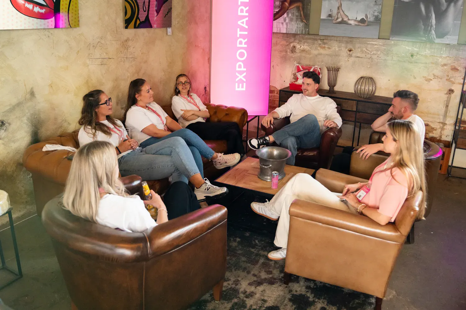 Gruppe von Eventteilnehmern im Loungebereich mit Ledersesseln vor Exportarts-Branding