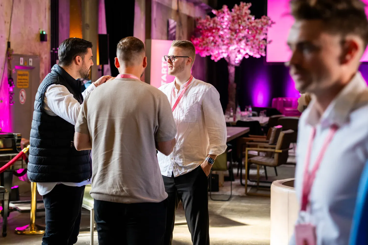 Drei Eventteilnehmer im Networking-Gespräch in Industrielocation mit pinker Beleuchtung