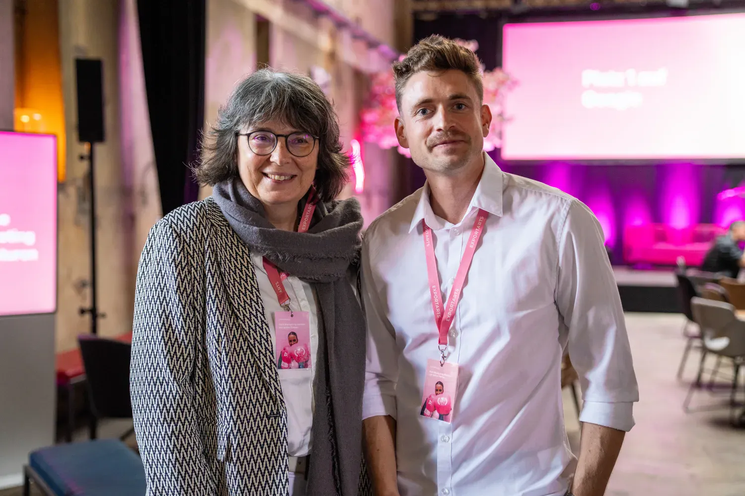 Zwei Eventteilnehmer mit pinken Exportarts-Lanyards posieren gemeinsam für Portraitfoto