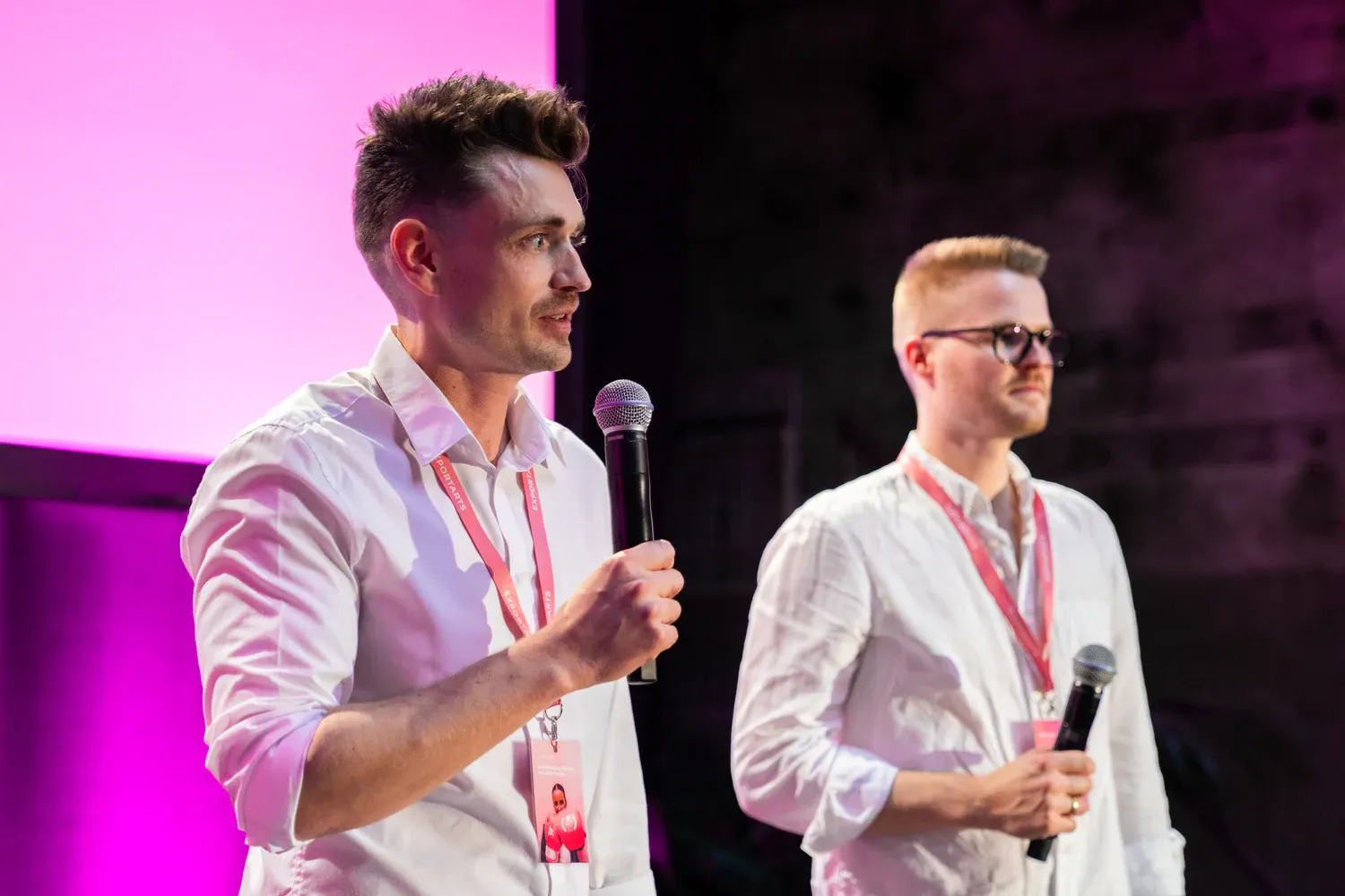 Zwei Speaker mit Mikrofonen auf der Bühne präsentieren gemeinsam