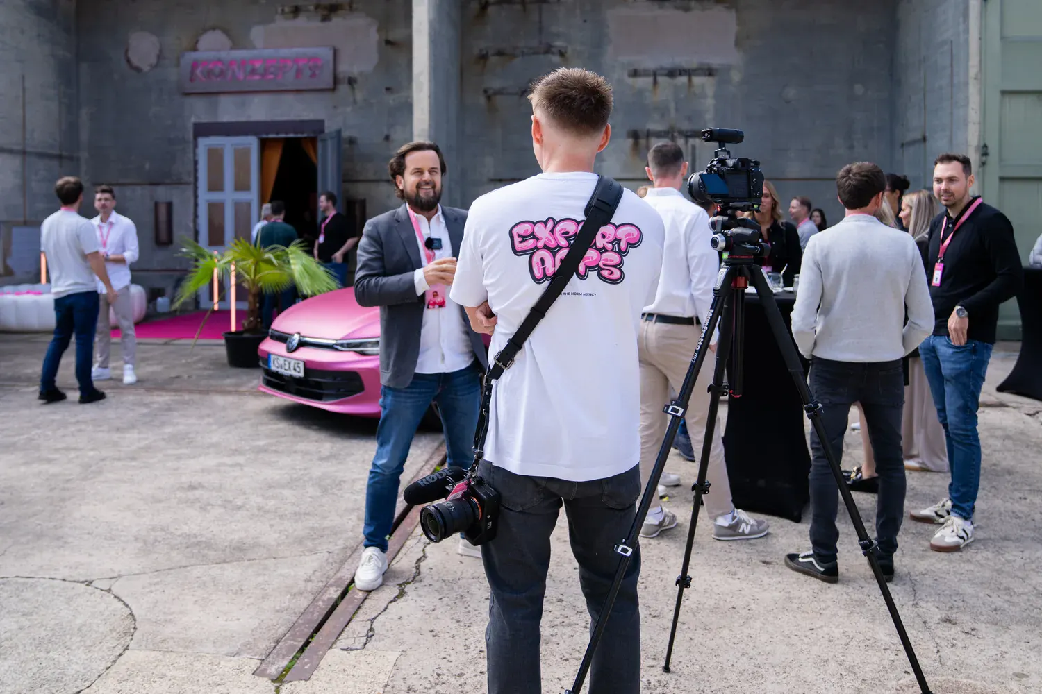 Kameramann mit Exportarts-Shirt filmt Interview vor pinkem VW Golf im Außenbereich der Eventlocation