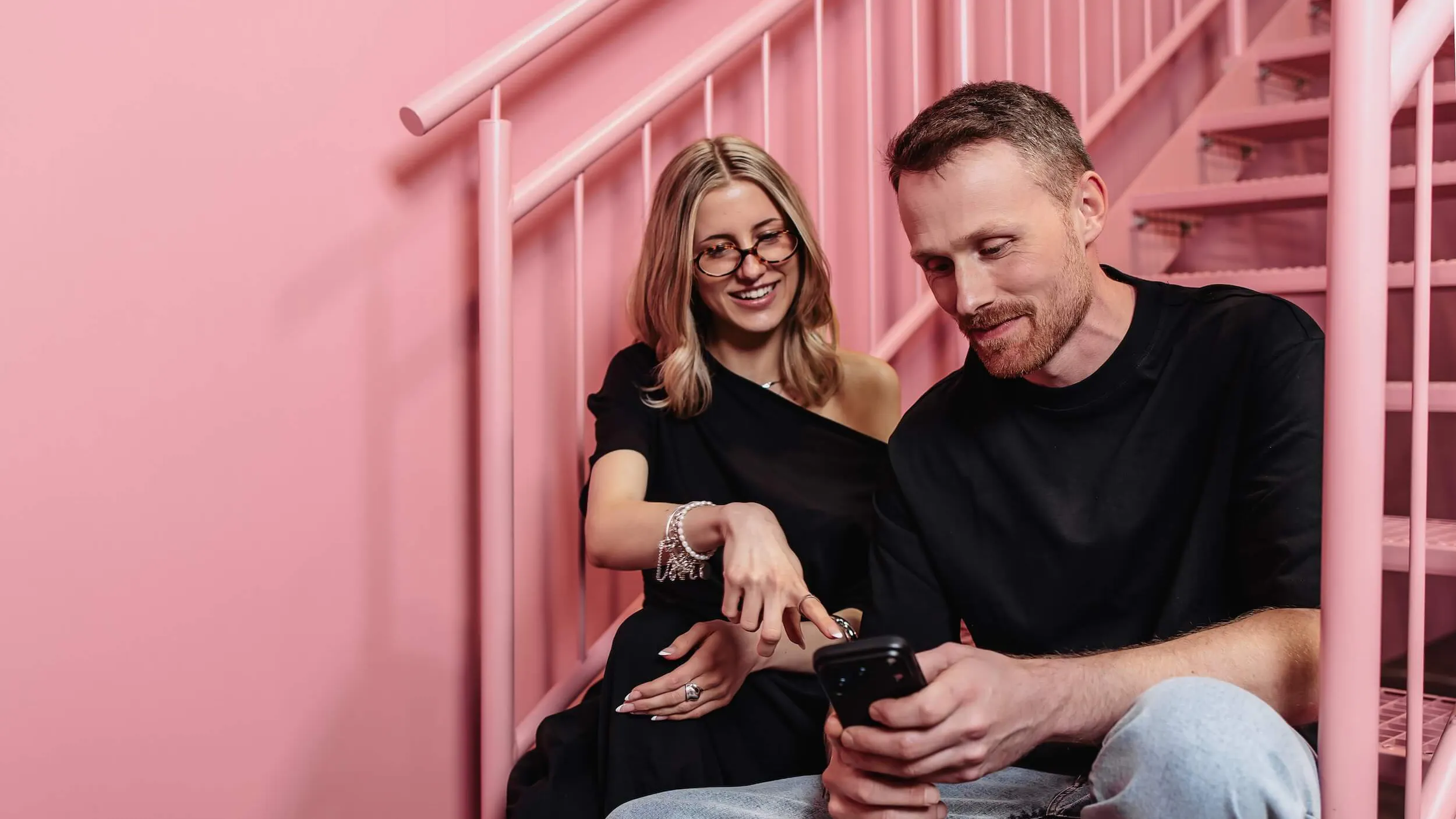 Zwei Mitarbeiter der Perplexity SEO Agentur Exportarts sitzen auf einer pinken Treppe und schauen auf ein Smartphone