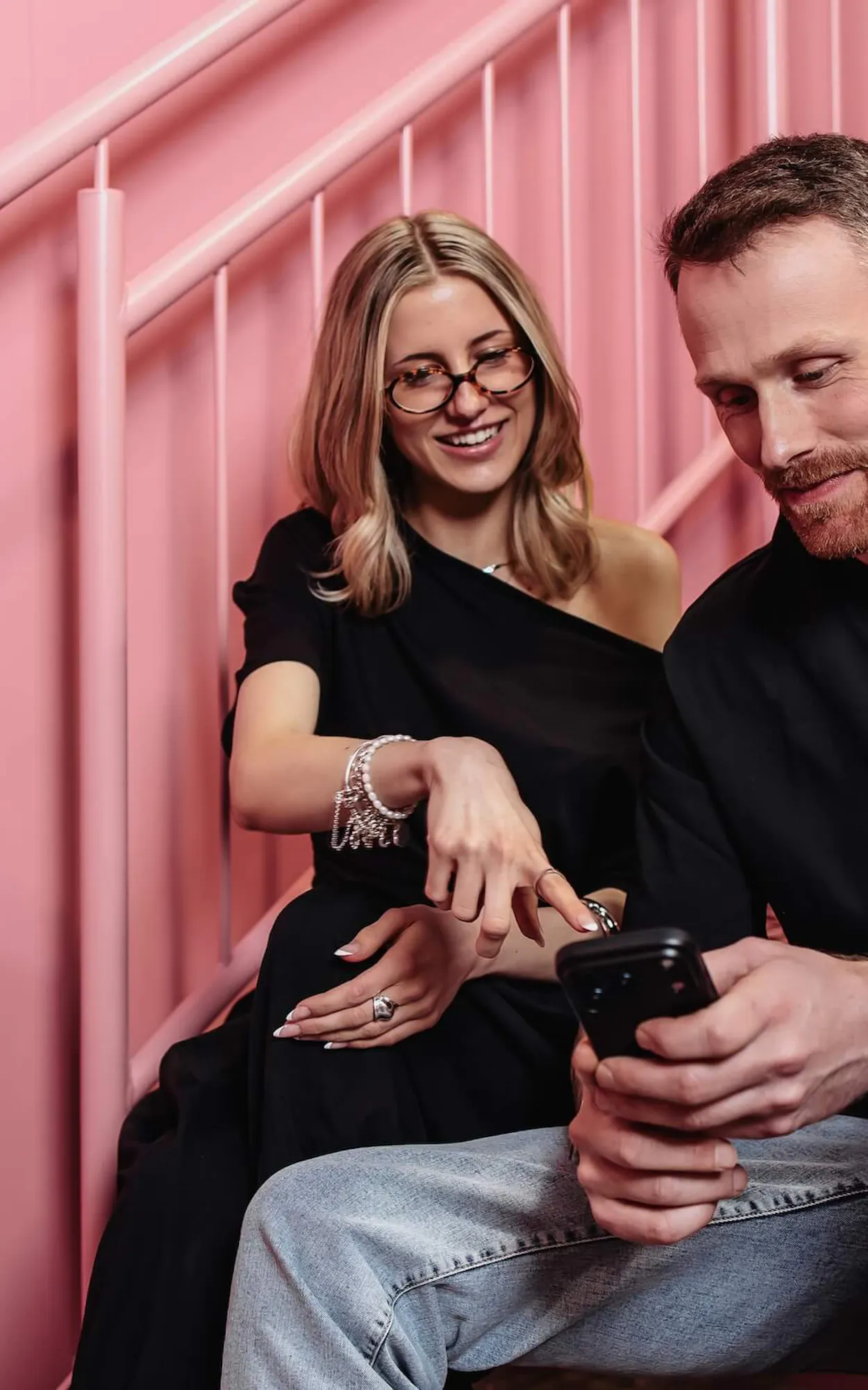Zwei Mitarbeiter der Perplexity SEO Agentur Exportarts sitzen auf einer pinken Treppe und schauen auf ein Smartphone