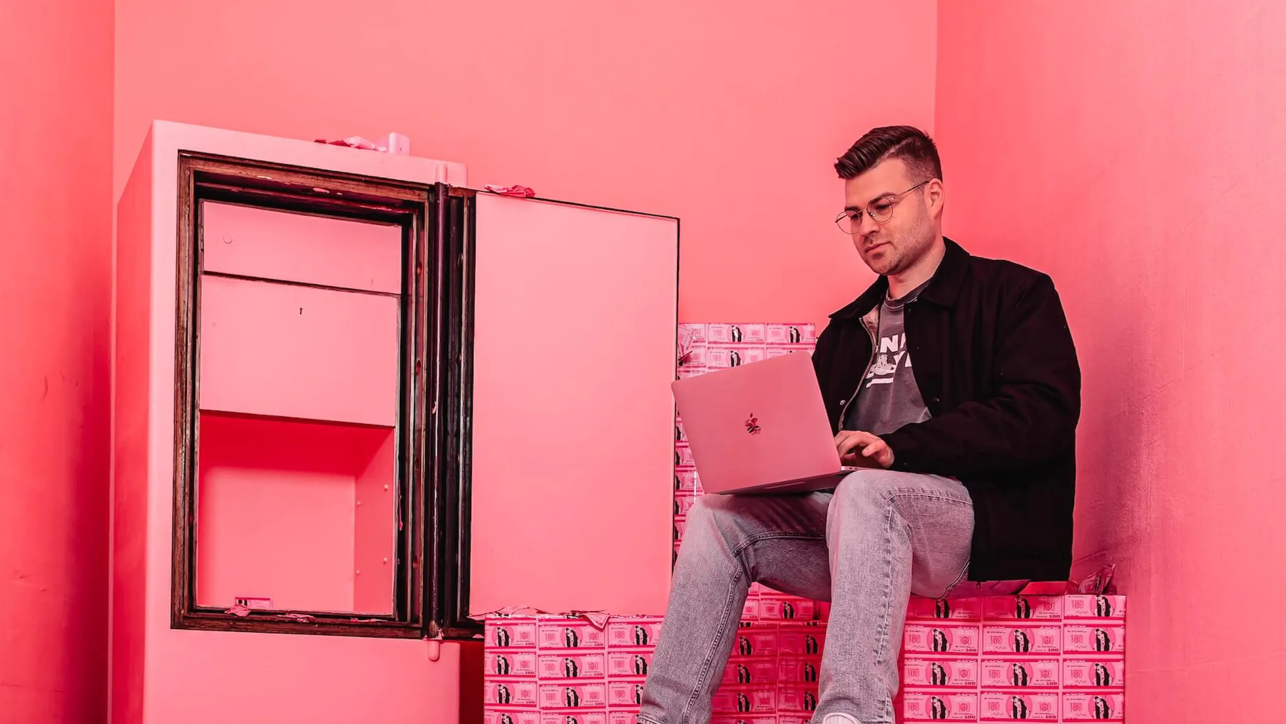 Luca von der Agentur Exportarts sitzt in einem pinken Tresor und arbeitet an einem Macbook