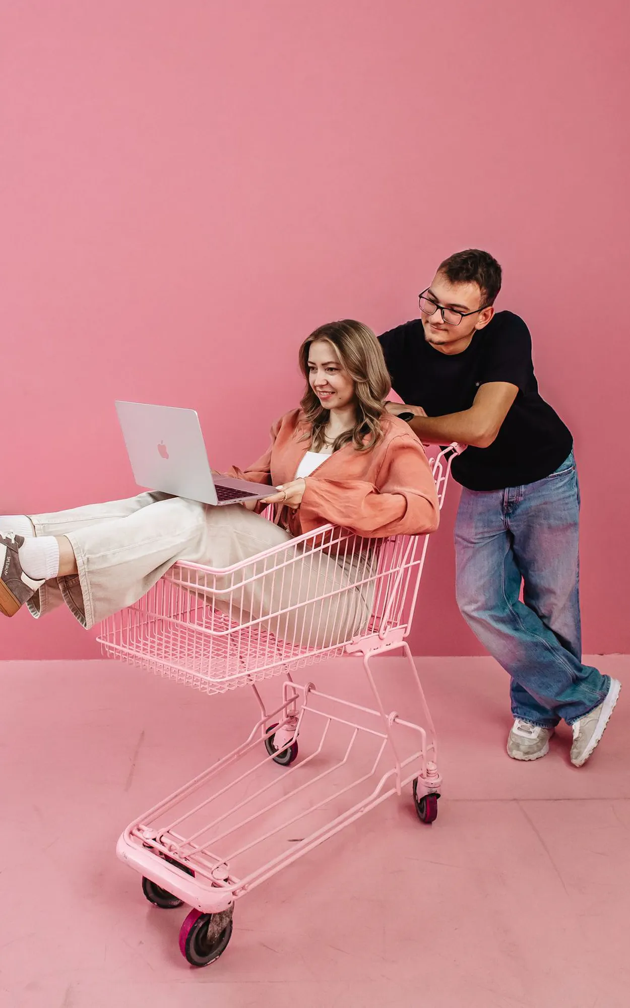 Exportarts Mitarbeiter schiebt Kollegin in einem pinken Einkaufswagen