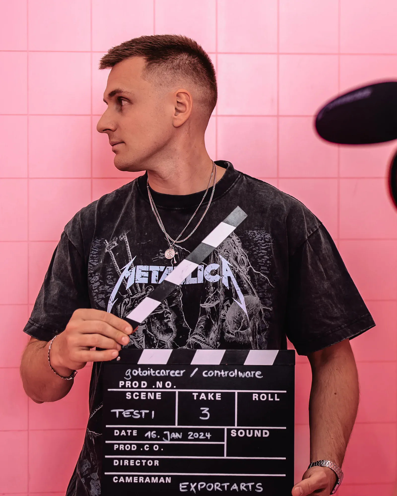 Exportarts-Mitarbeiter hält eine Filmklappe vor pinker Fliesenwand