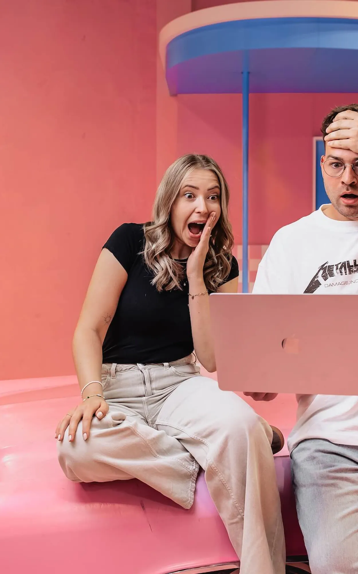Zwei Mitarbeiter der SEO Copywriting Agentur sitzen auf einem pinken Auto und schauen schockiert in ein Macbook
