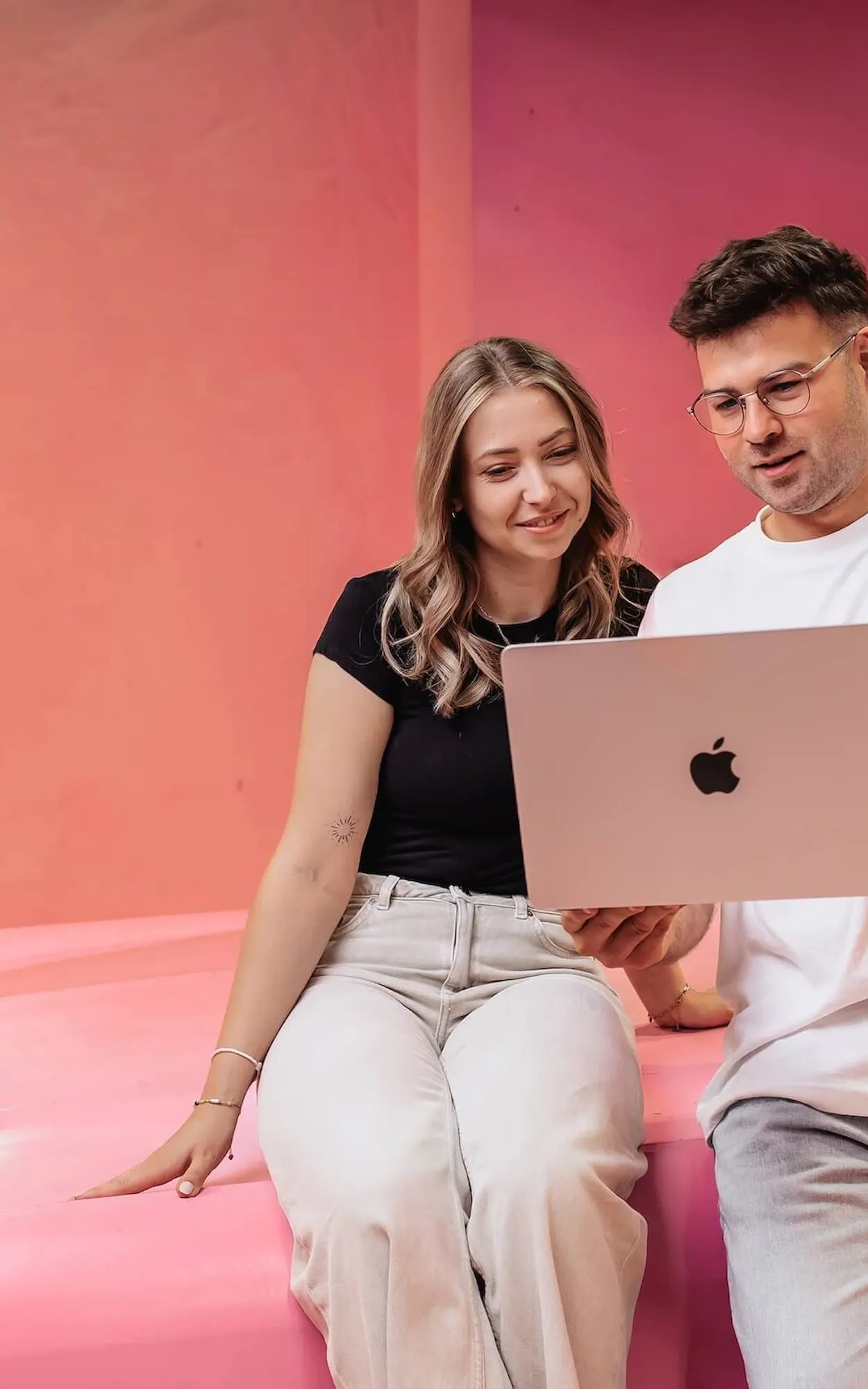 Zwei Mitarbeiter der Website Agentur Exportarts sitzen auf einem pinken Auto und schauen auf einen Laptop