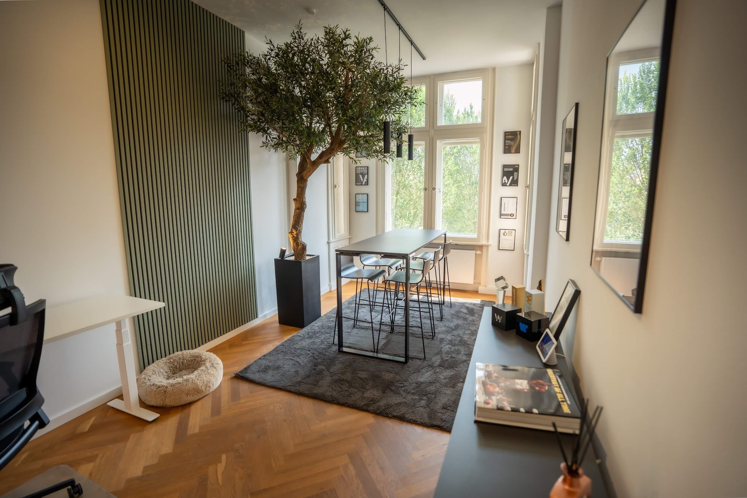 Meetingbereich im Exportarts Büro mit Stehtisch, Barhockern und dekorativem Baum