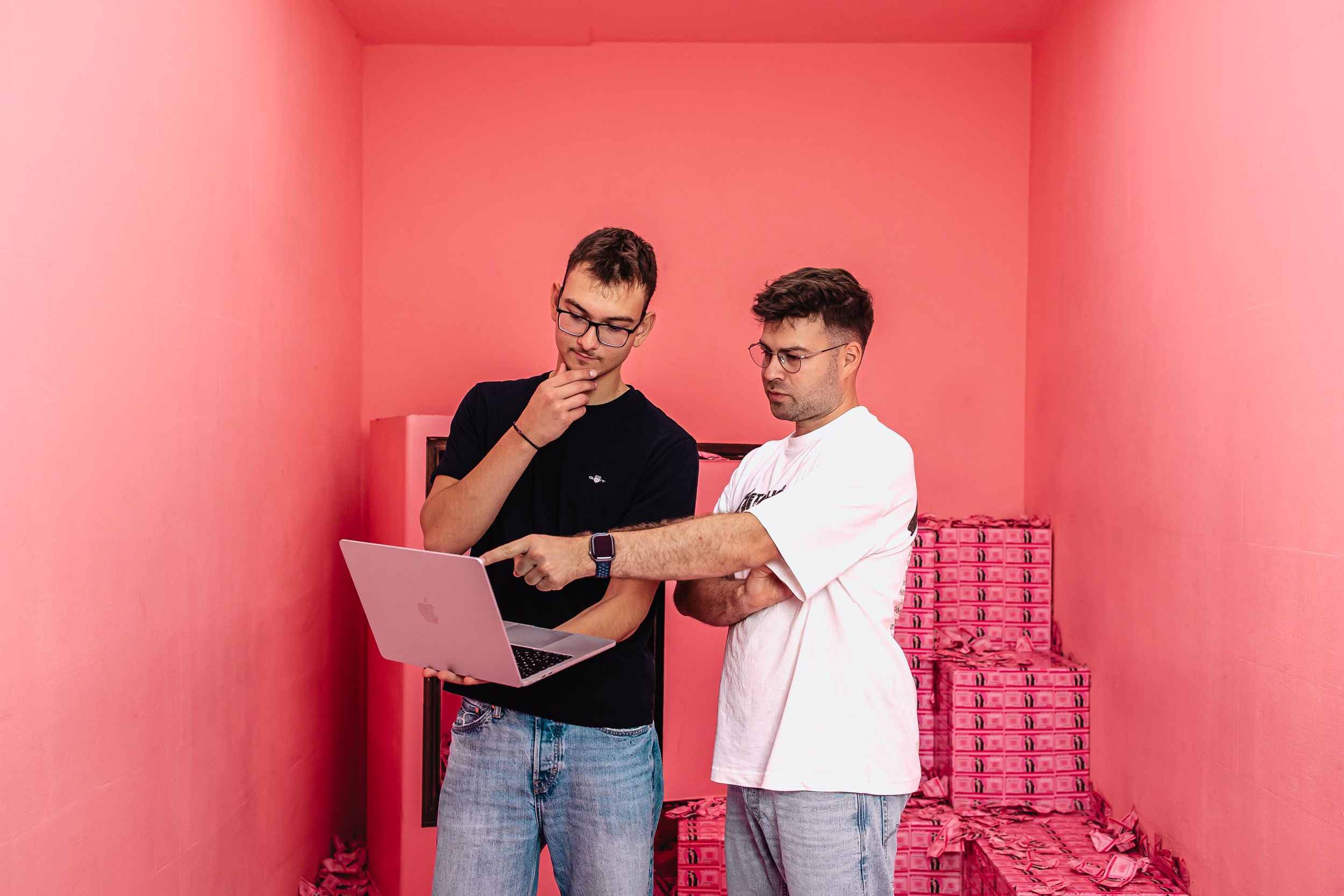 Zwei Webentwickler von Exportarts stehen in einem pinken Raum und schauen auf einen Laptop