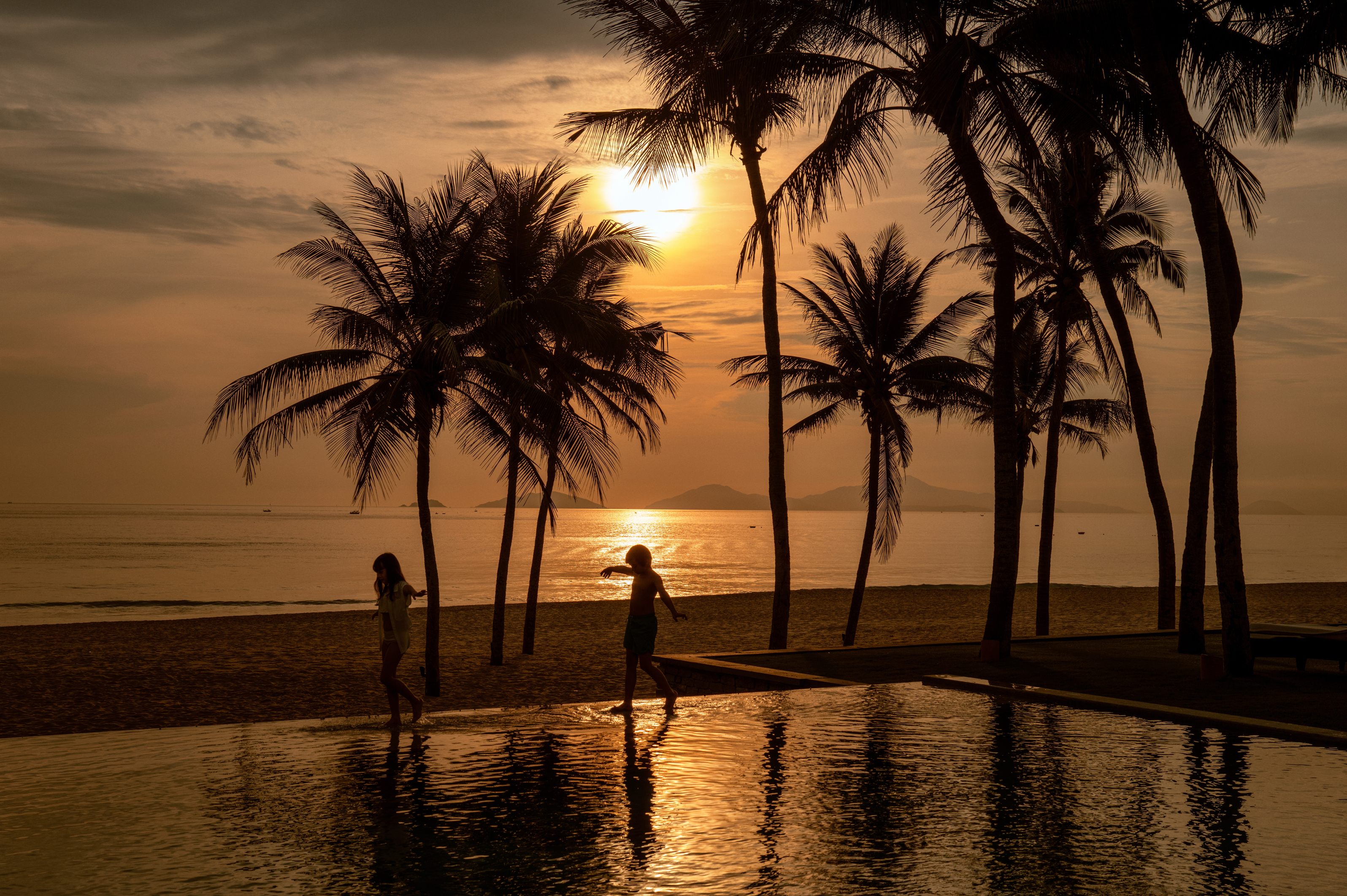 Children silhouetted at infinity pool during golden sunset, Hoi An Vietnam