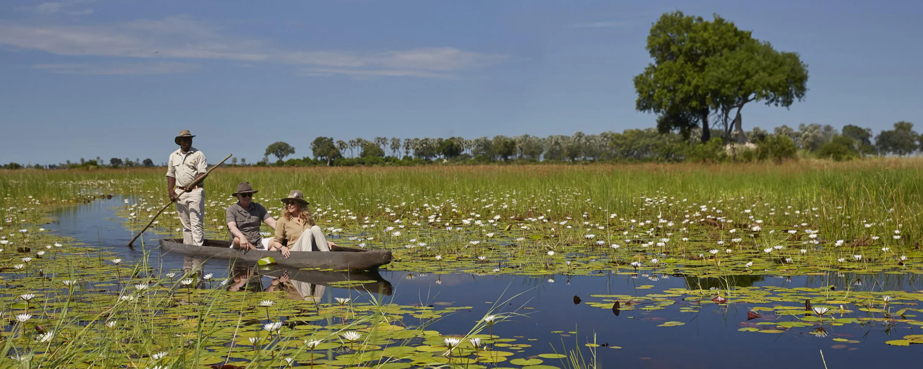 Guests glide by mokoro through a lily-covered Okavango Delta channel, poled by a local guide.