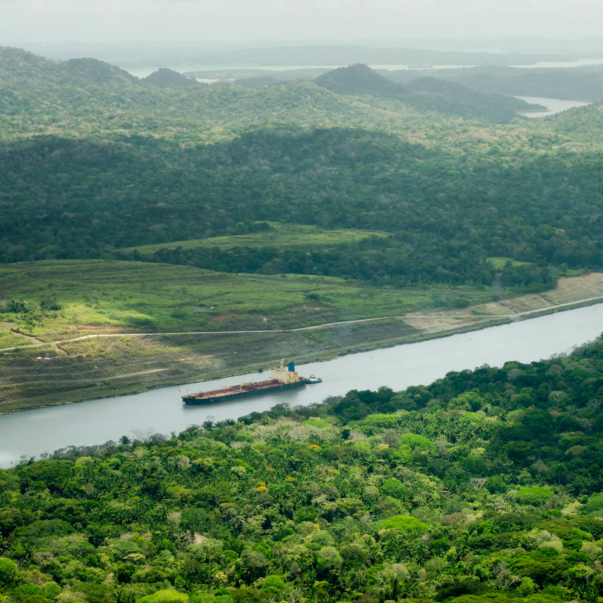 Aerial view of a cargo ship transiting the Panama Canal through rainforest