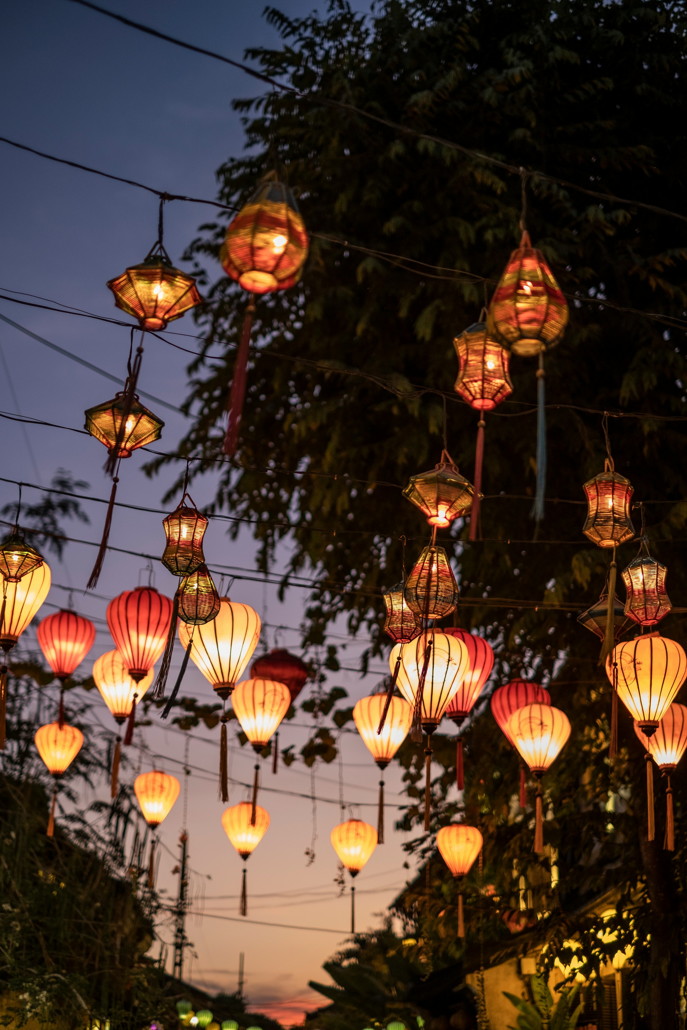 Strands of glowing lanterns are hung criss-cross above a street at sunset