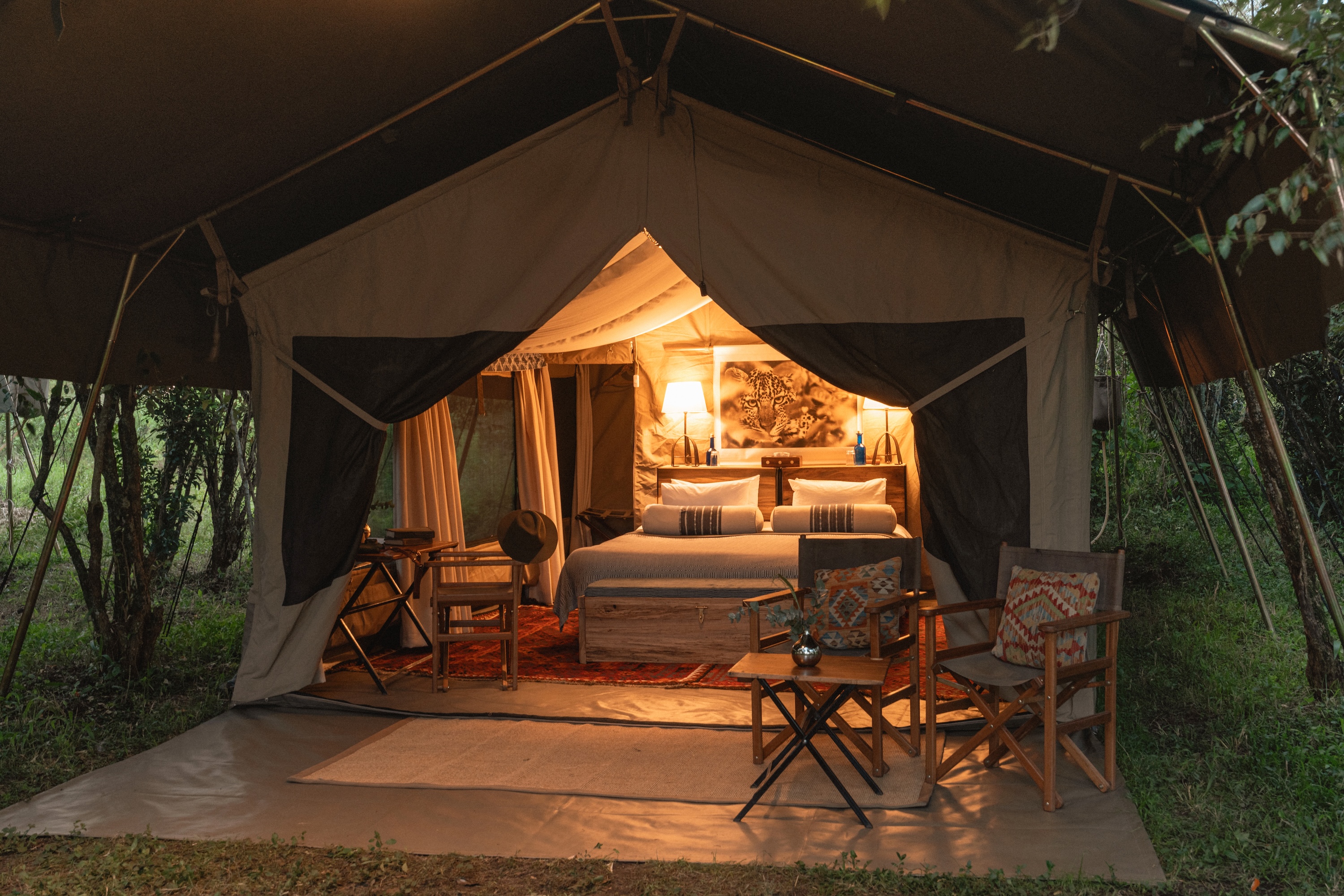 A warmly lit safari tent bedroom with a leopard print, twin lamps, and a kilim rug.