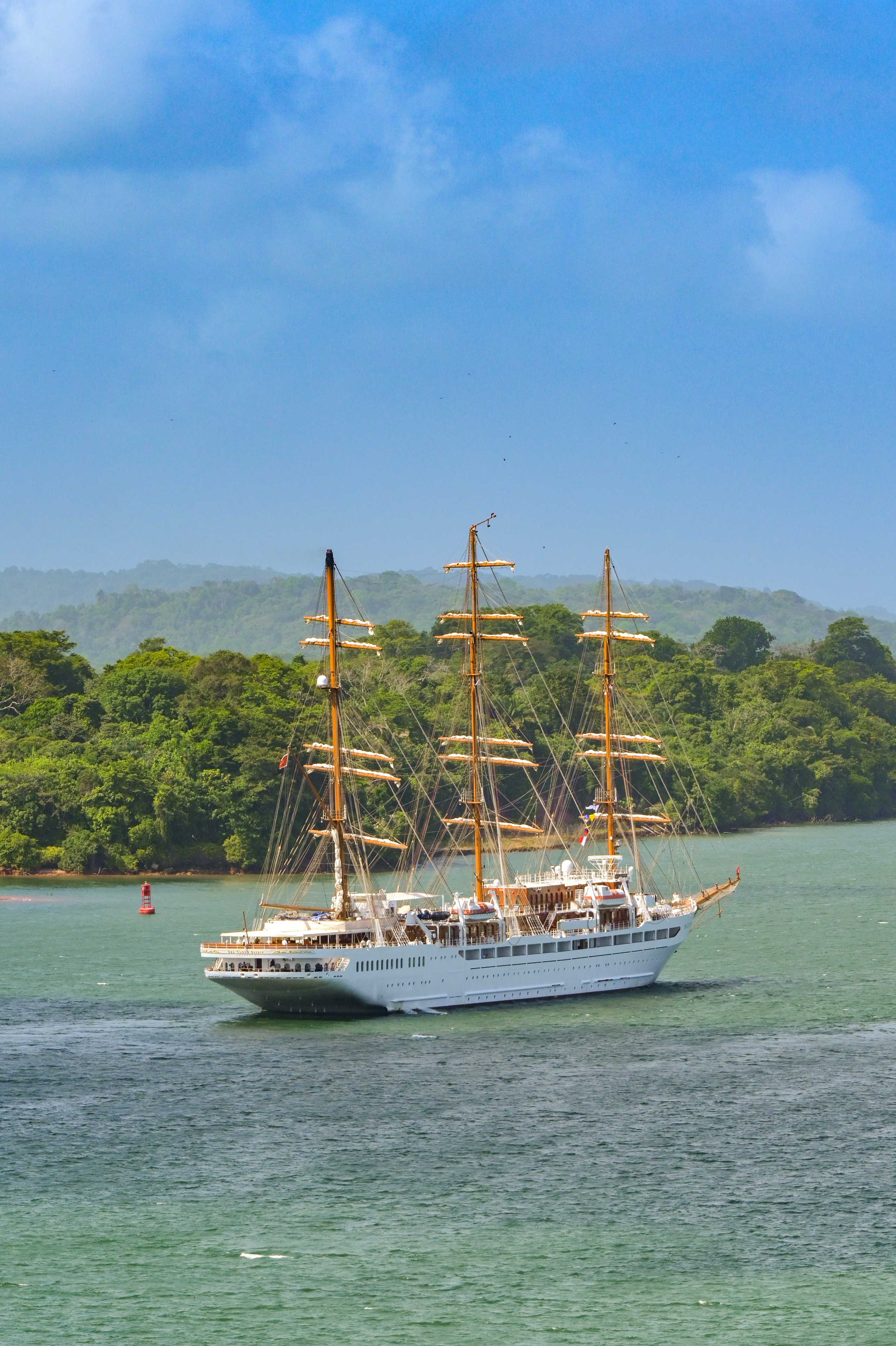 Tall-masted sailing cruise ship navigating the Panama Canal near the rainforest coastline