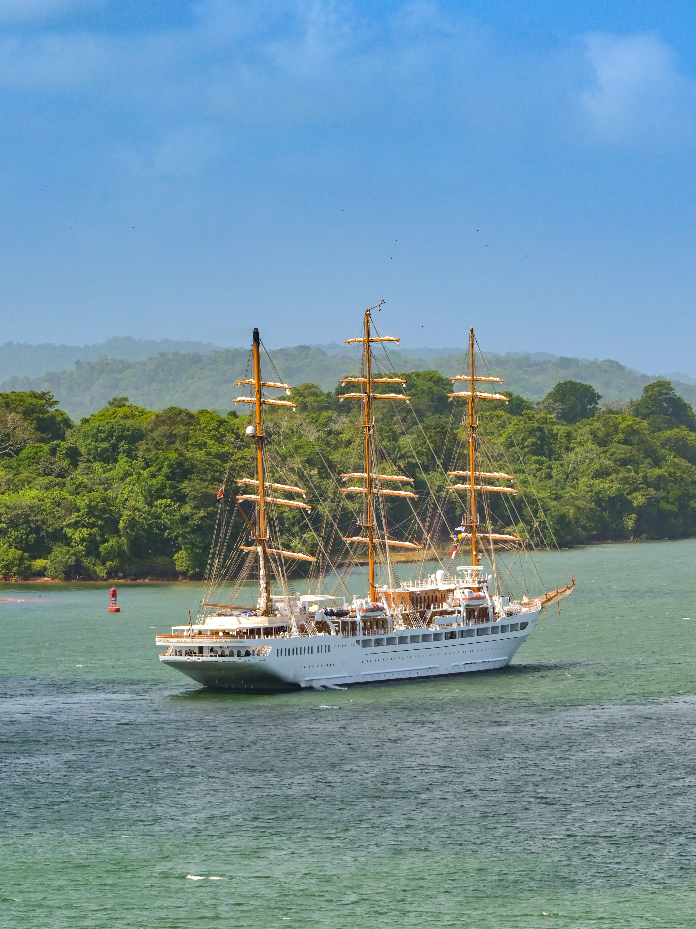 Tall-masted sailing cruise ship navigating the Panama Canal near the rainforest coastline