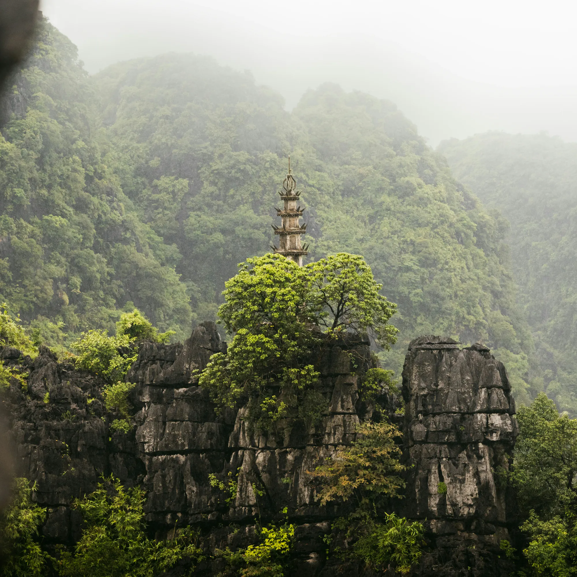 Ancient pagoda rising through misty limestone rocks, Ninh Binh Vietnam