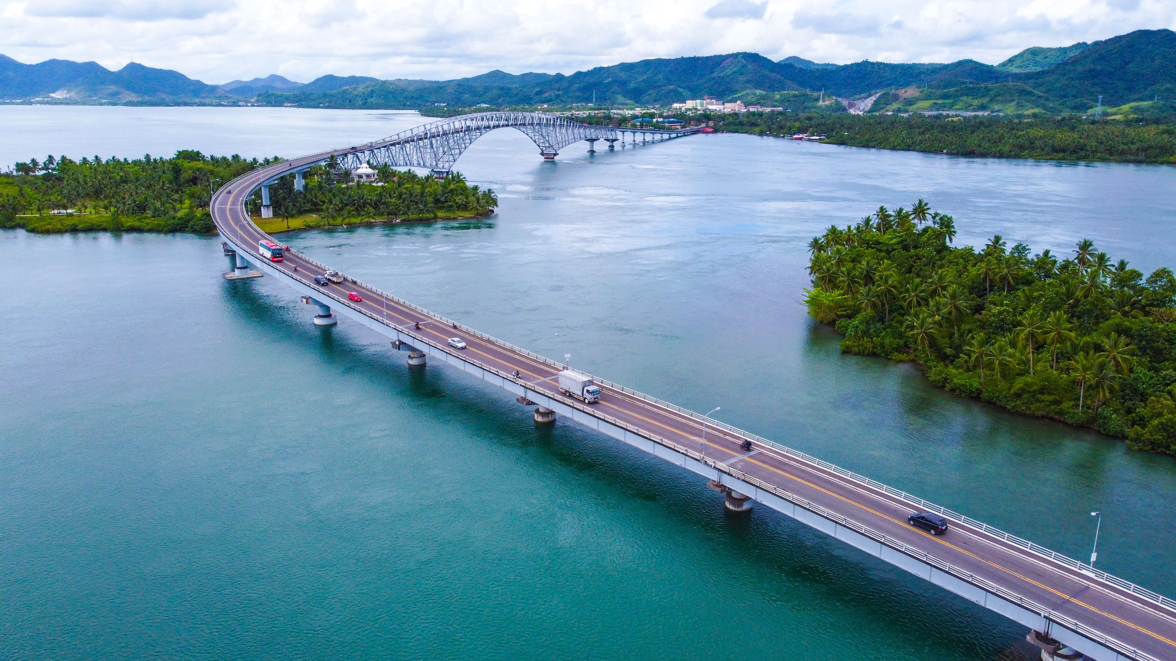 Arched bridge spanning a turquoise bay surrounded by mountains and palm trees