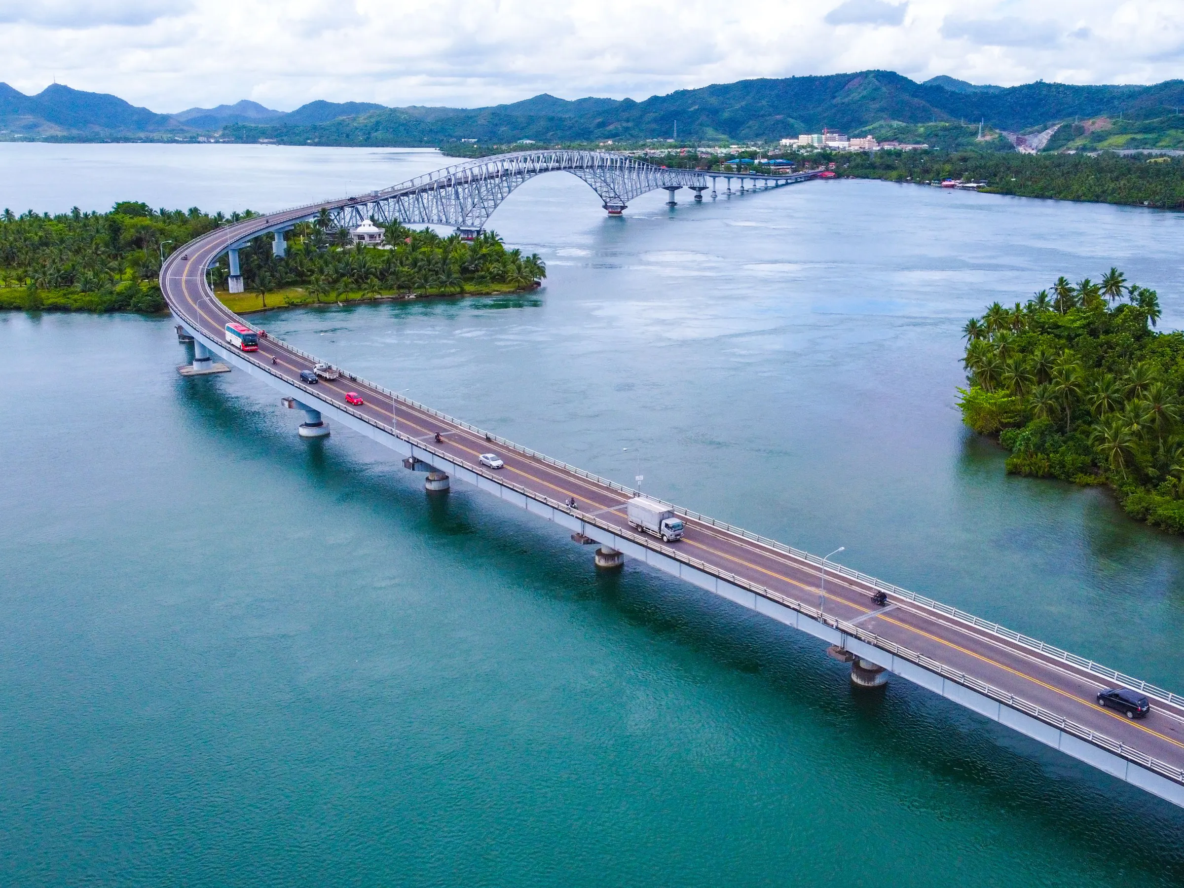 Arched bridge spanning a turquoise bay surrounded by mountains and palm trees