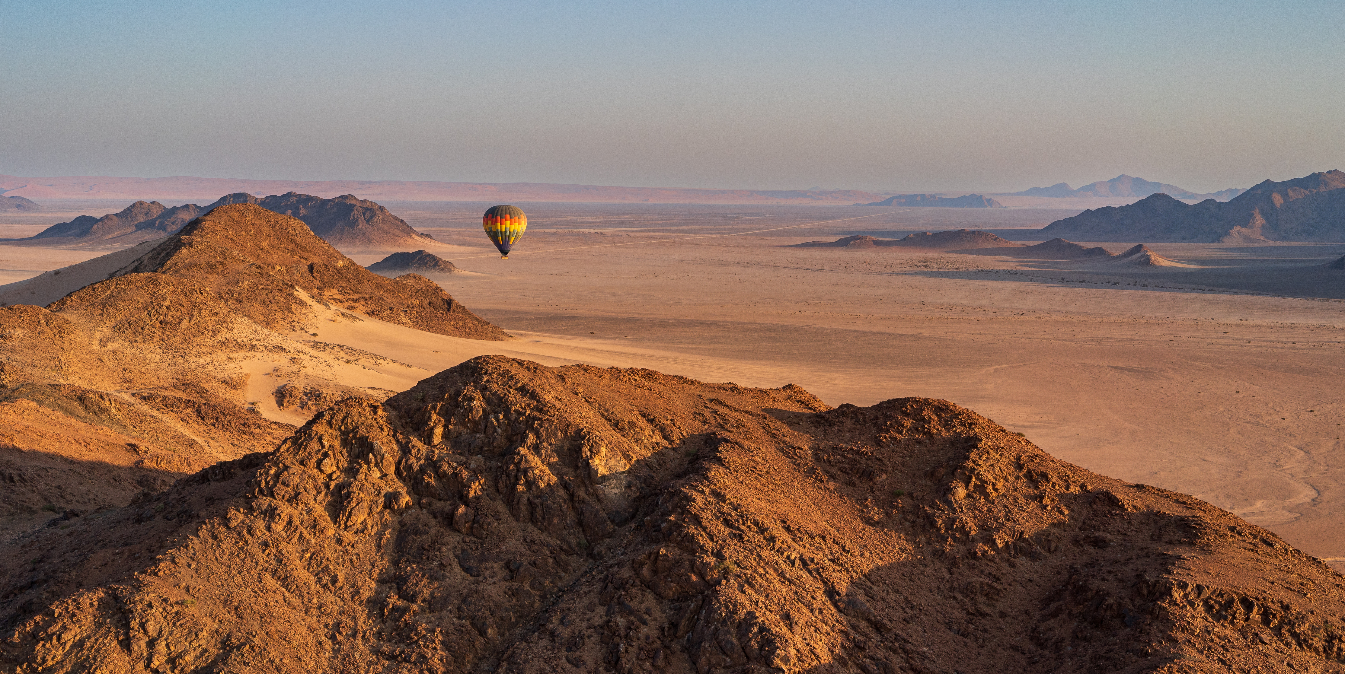 Hot air balloon drifting over rugged desert mountains in Namibia at dawn
