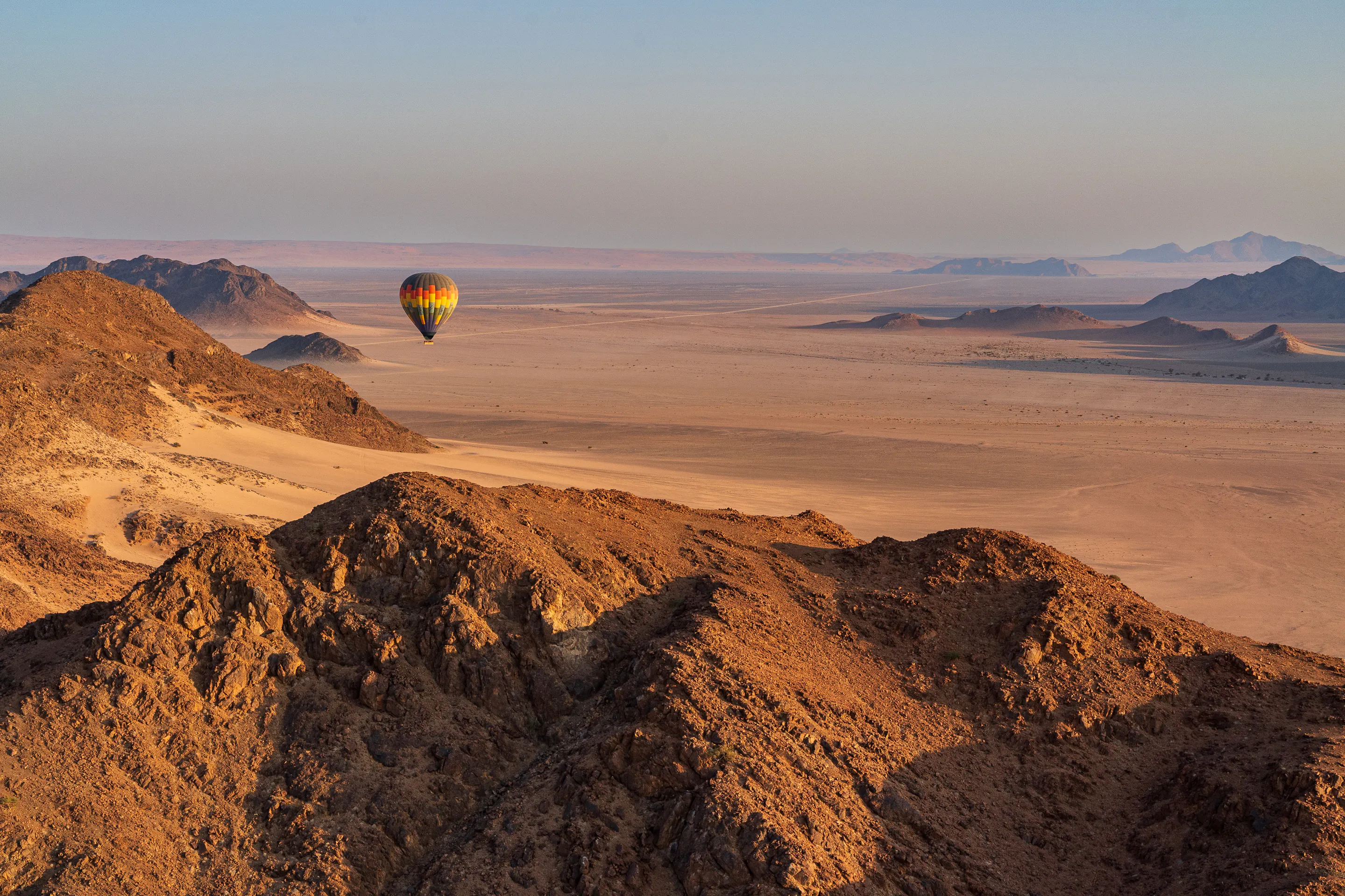 Hot air balloon drifting over rugged desert mountains in Namibia at dawn