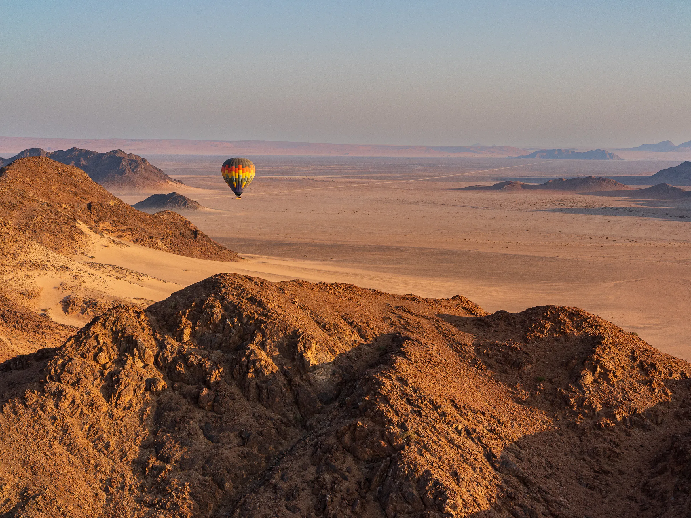 Hot air balloon drifting over rugged desert mountains in Namibia at dawn