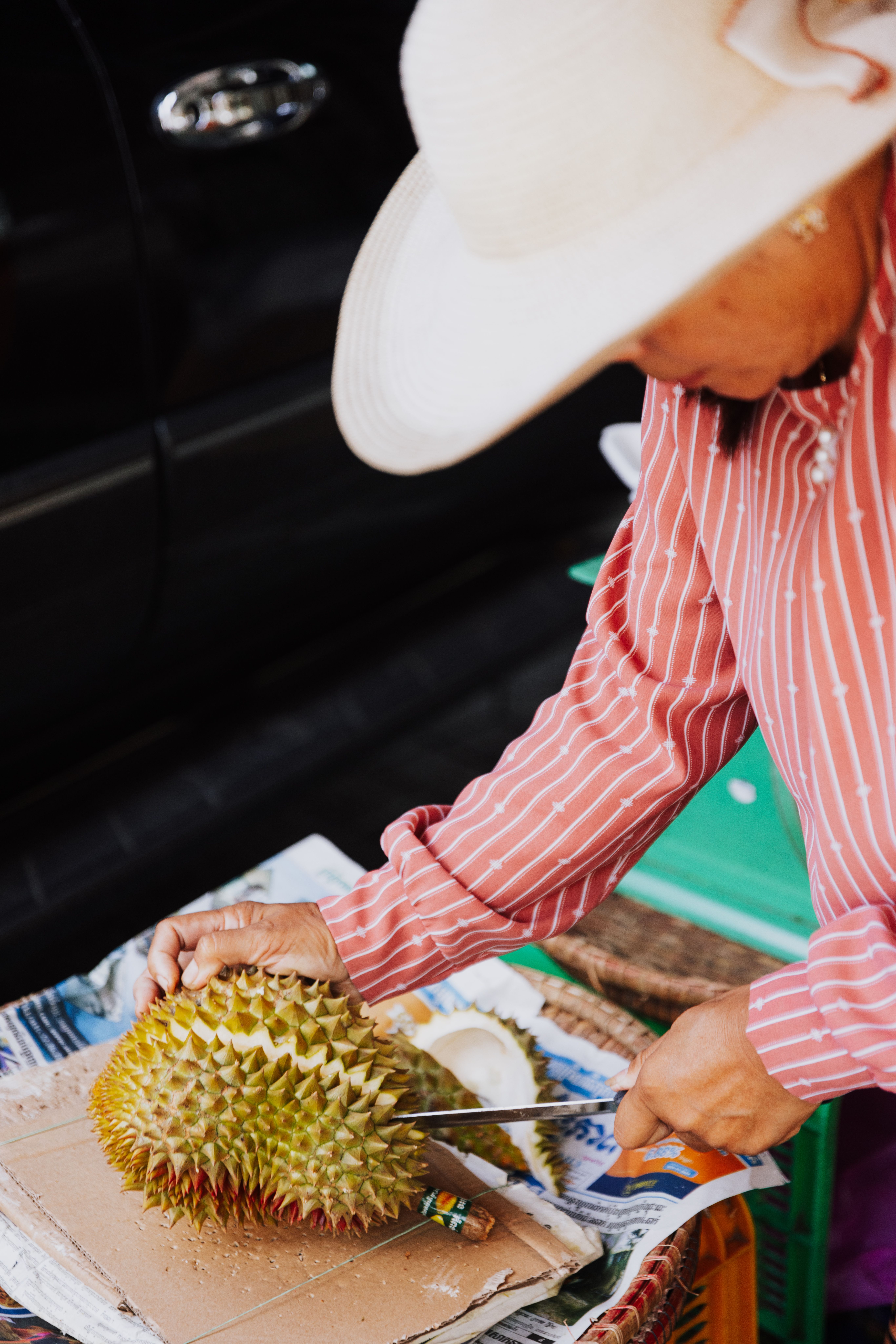 Local vendor in conical hat cutting fresh durian, Thailand