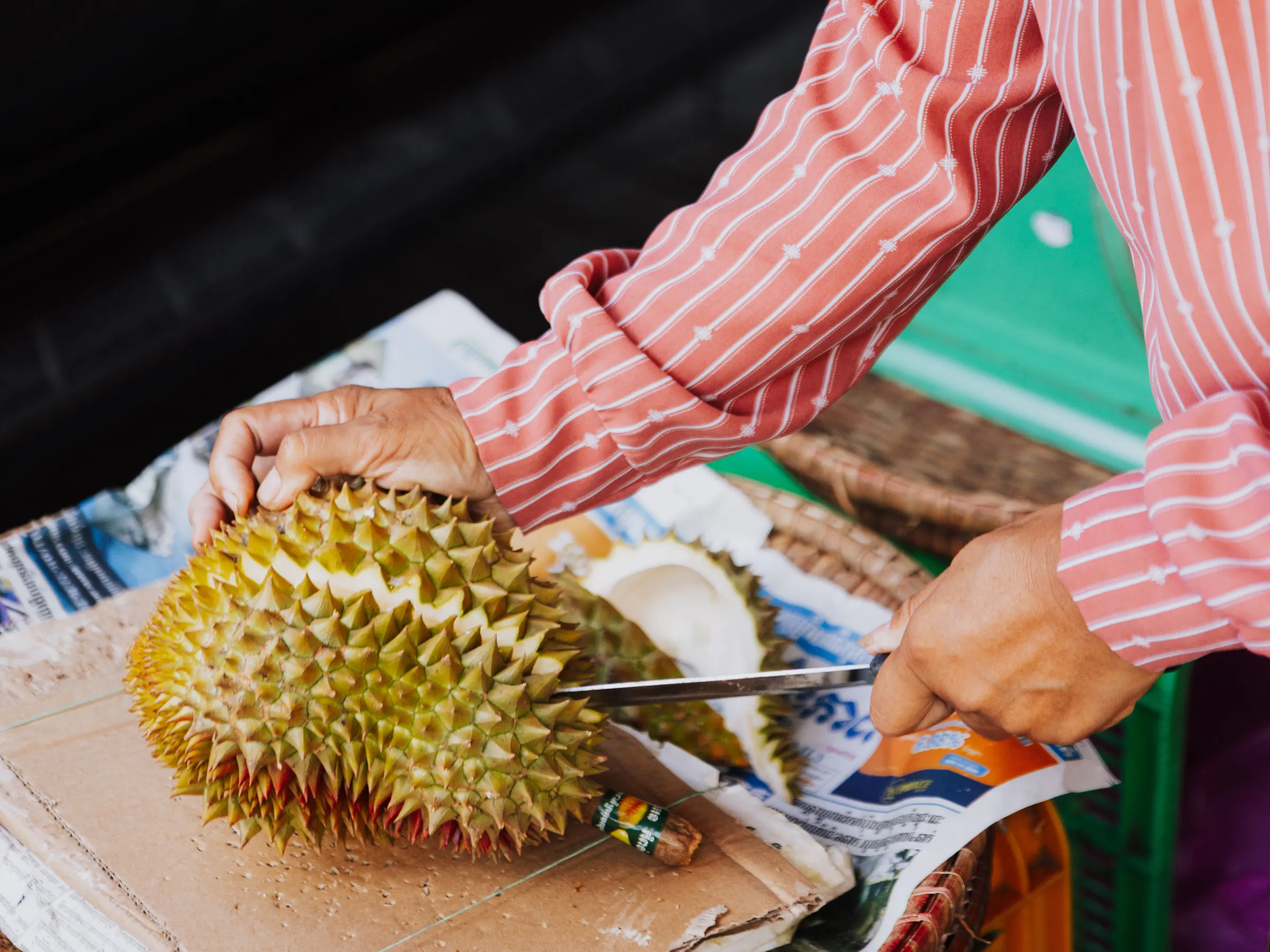 Local vendor in conical hat cutting fresh durian, Thailand
