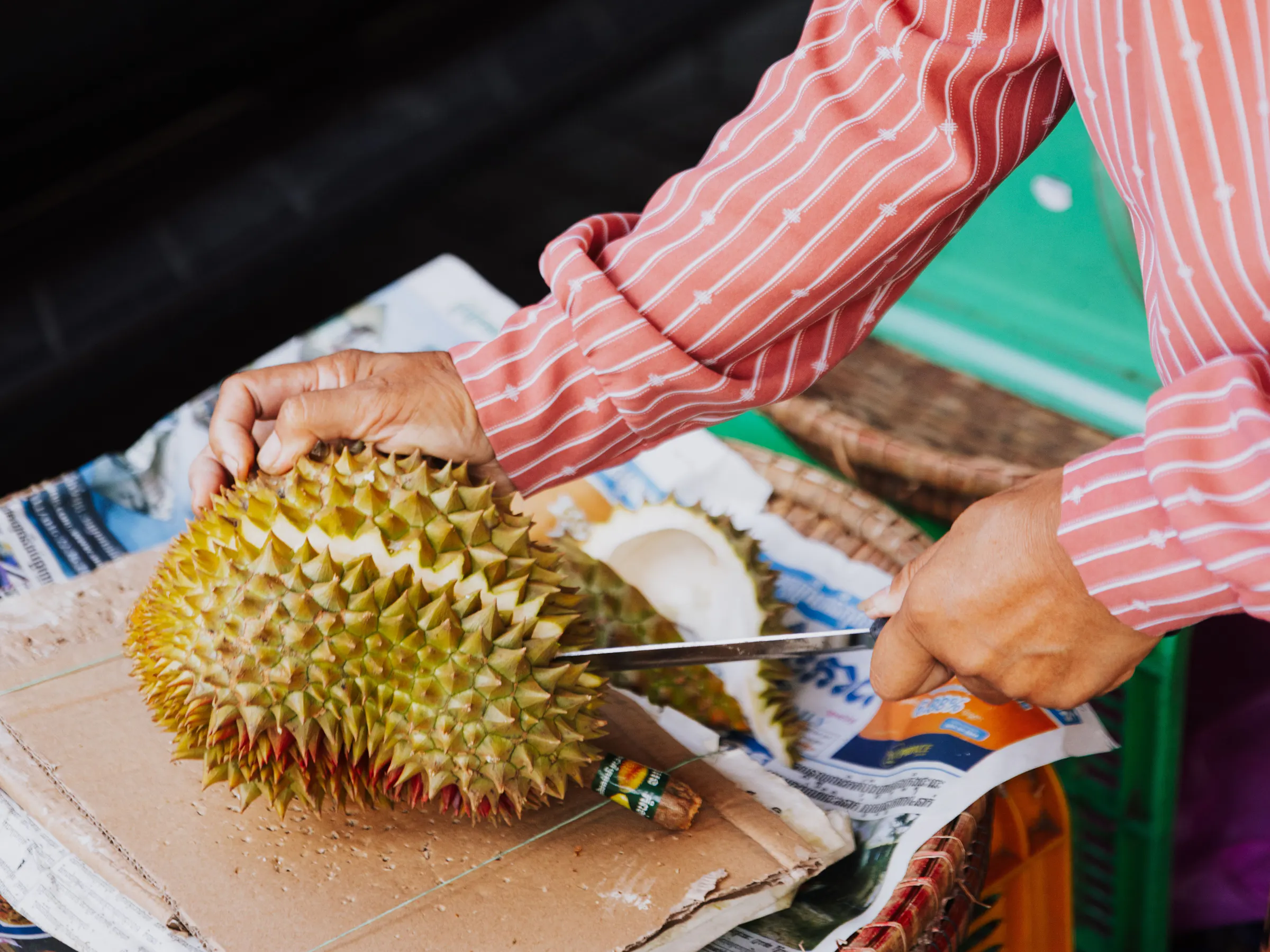 Local vendor in conical hat cutting fresh durian, Thailand