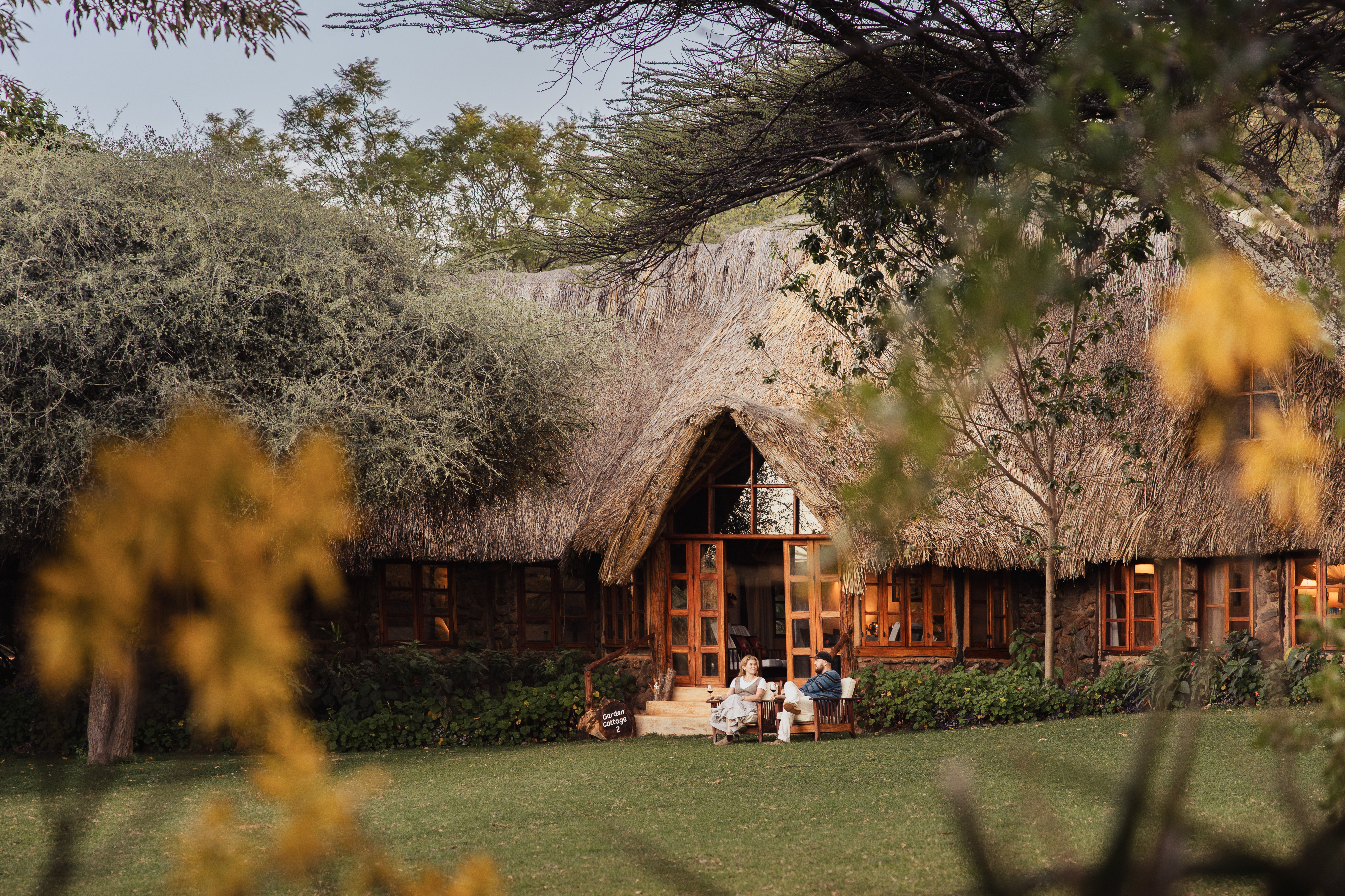 Guests relaxing outside a thatched-roof cottage at Lewa Wilderness, Laikipia, Kenya
