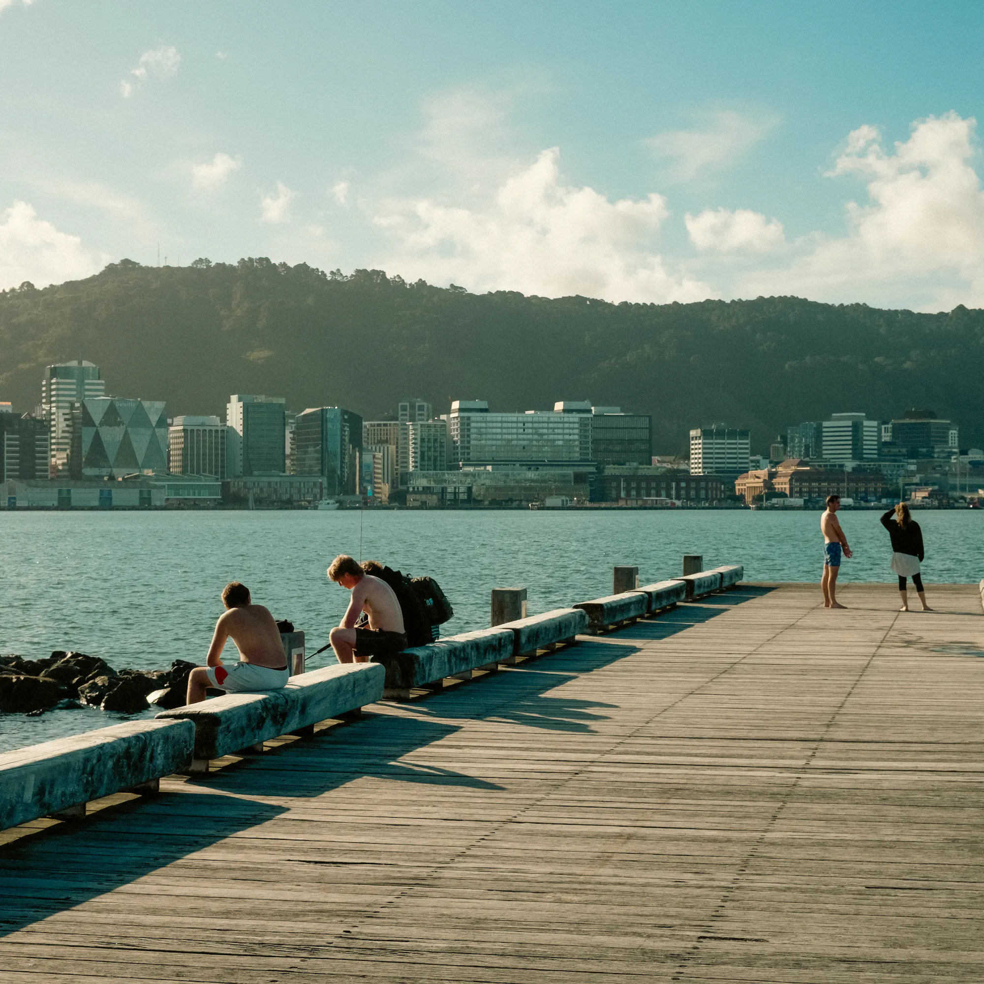 People relaxing on waterfront pier with Wellington CBD skyline beyond