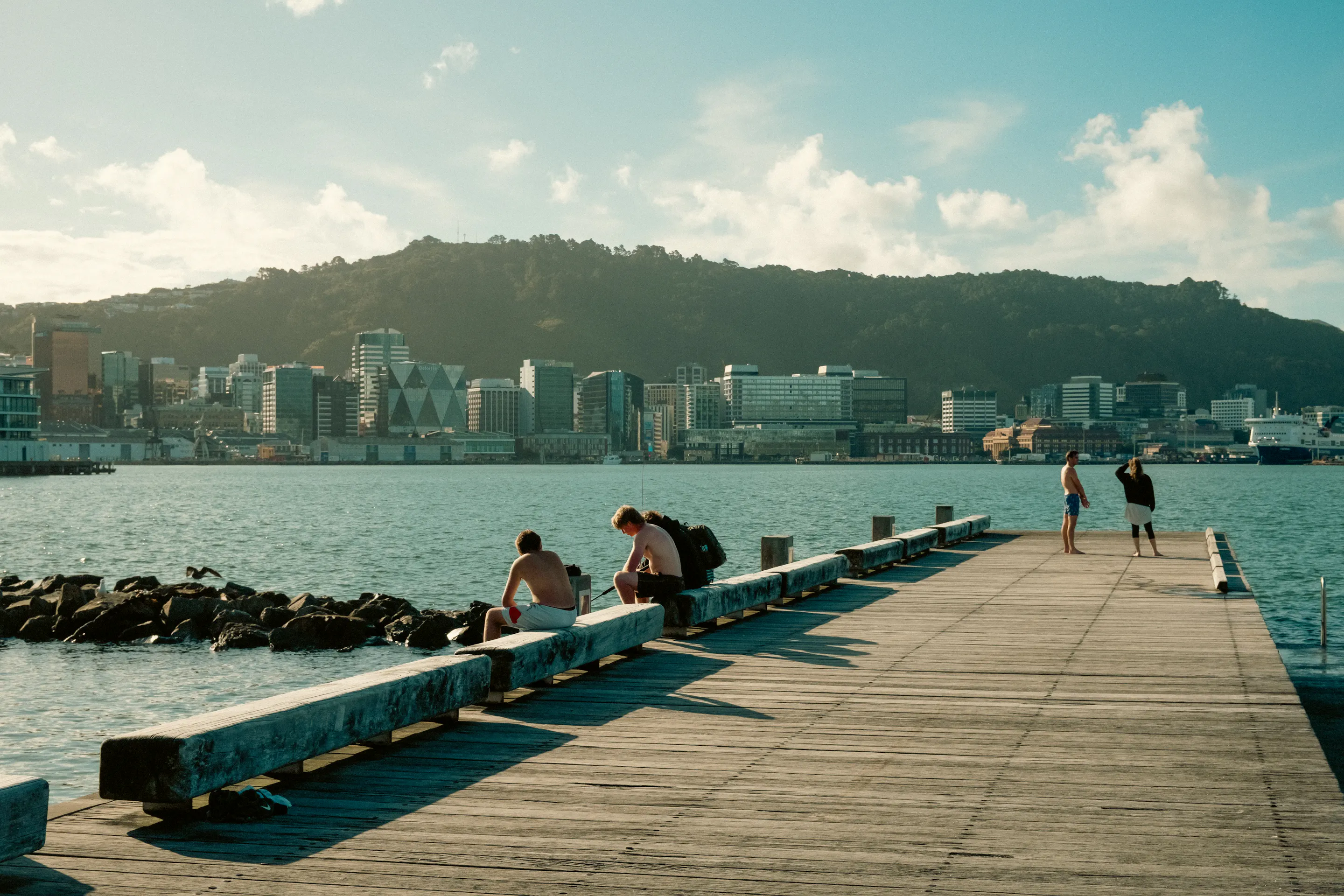 People relaxing on waterfront pier with Wellington CBD skyline beyond