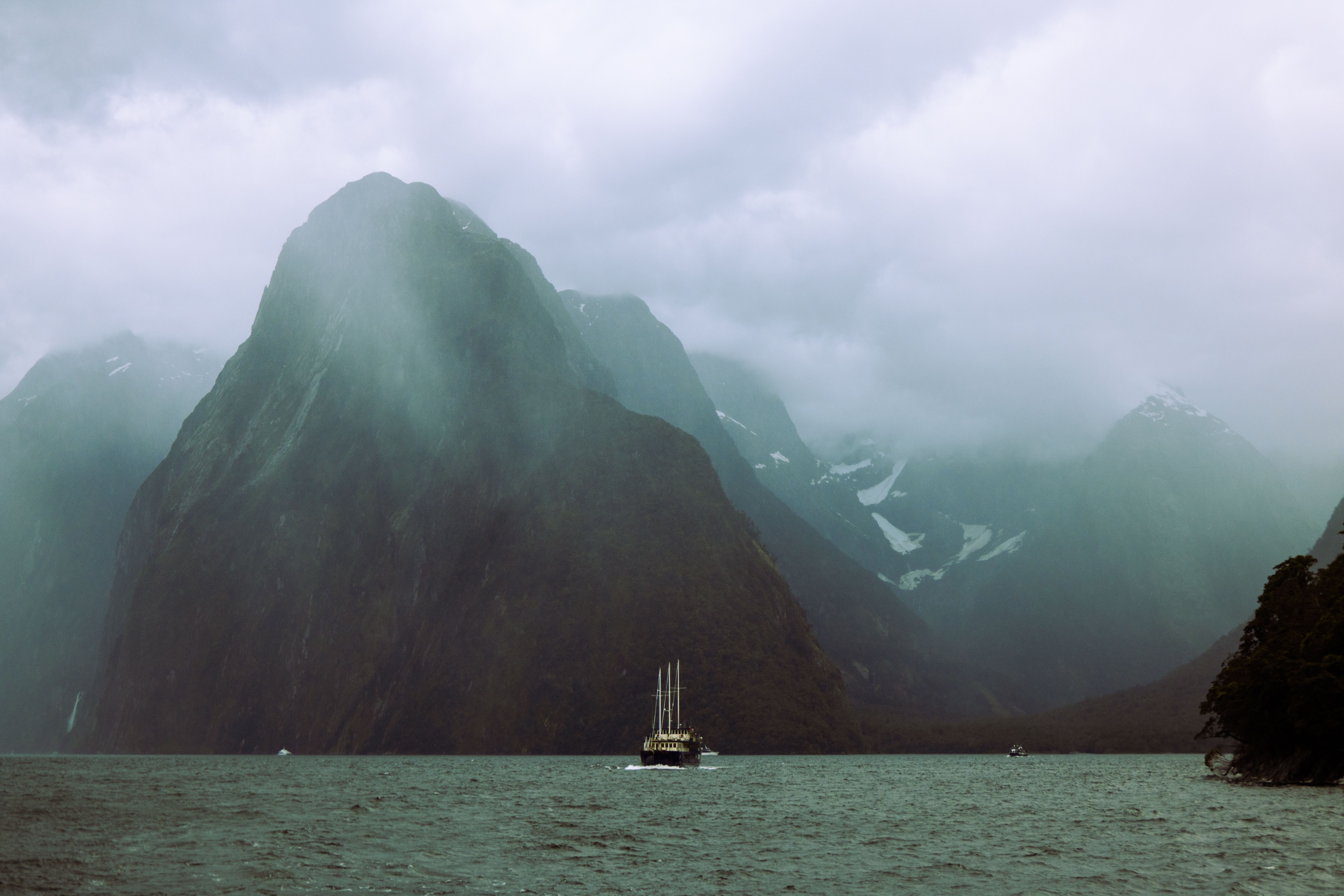 Boat sailing beneath Mitre Peak in misty Milford Sound, New Zealand