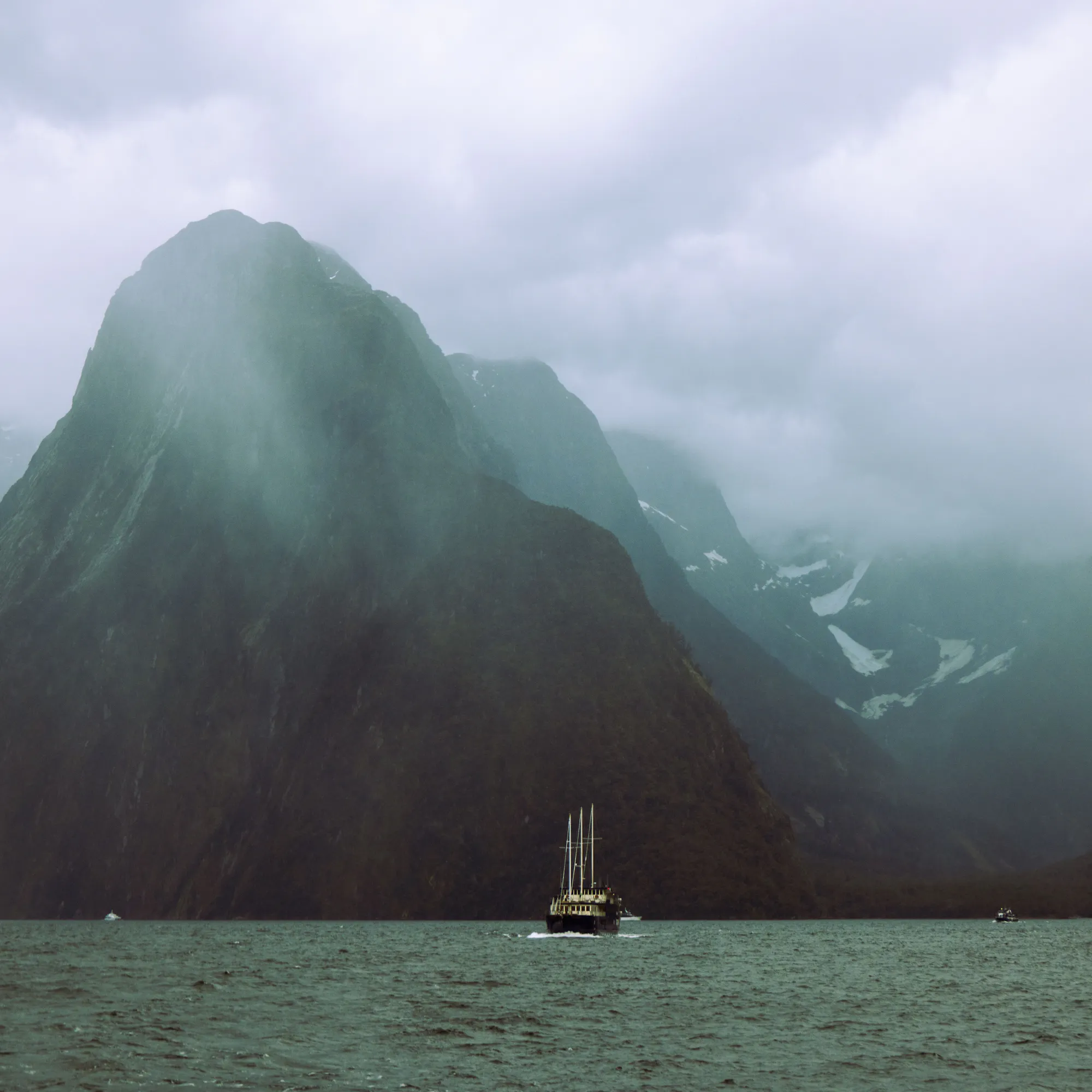 Boat sailing beneath Mitre Peak in misty Milford Sound, New Zealand