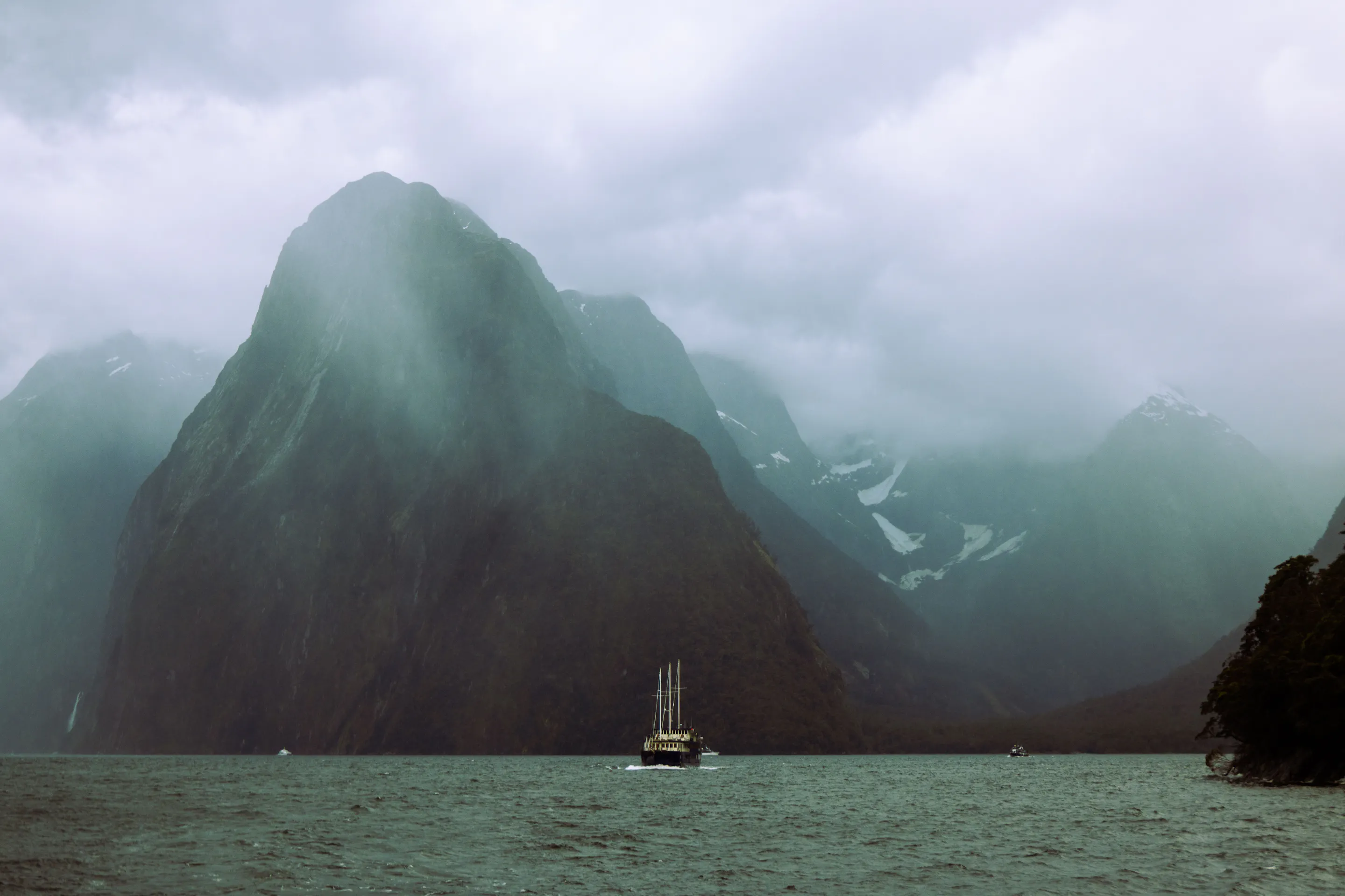 Boat sailing beneath Mitre Peak in misty Milford Sound, New Zealand