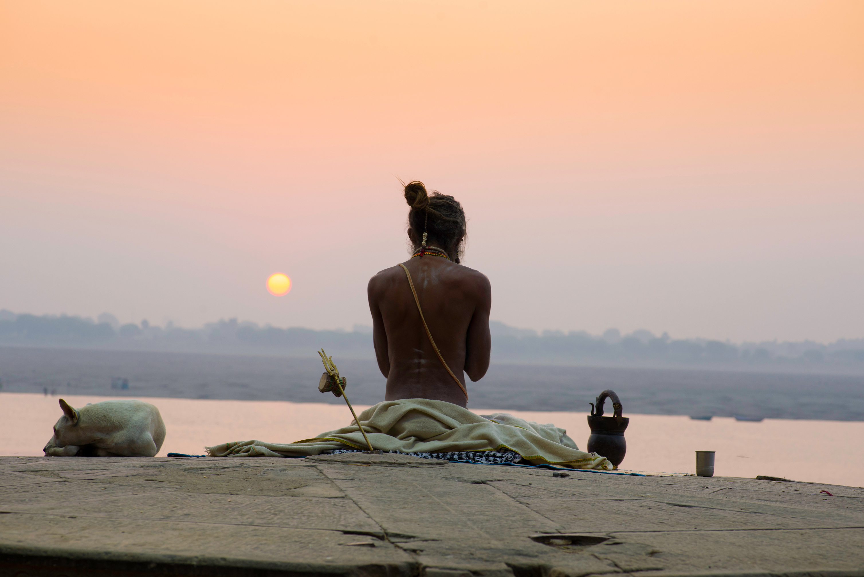 Sadhu meditating at sunrise on the Ganges ghats in Varanasi, India, with a sleeping dog nearby