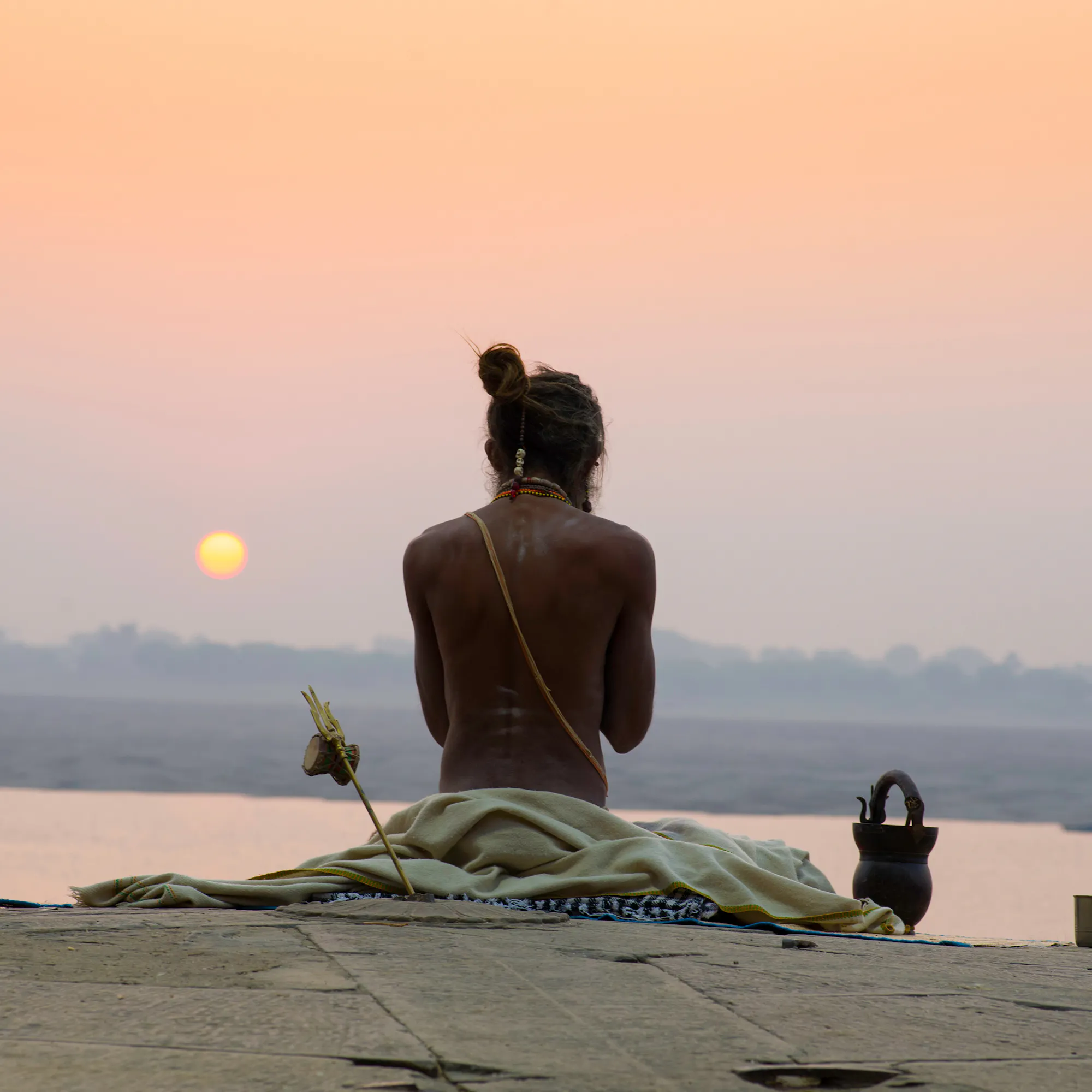 Sadhu meditating at sunrise on the Ganges ghats in Varanasi, India, with a sleeping dog nearby