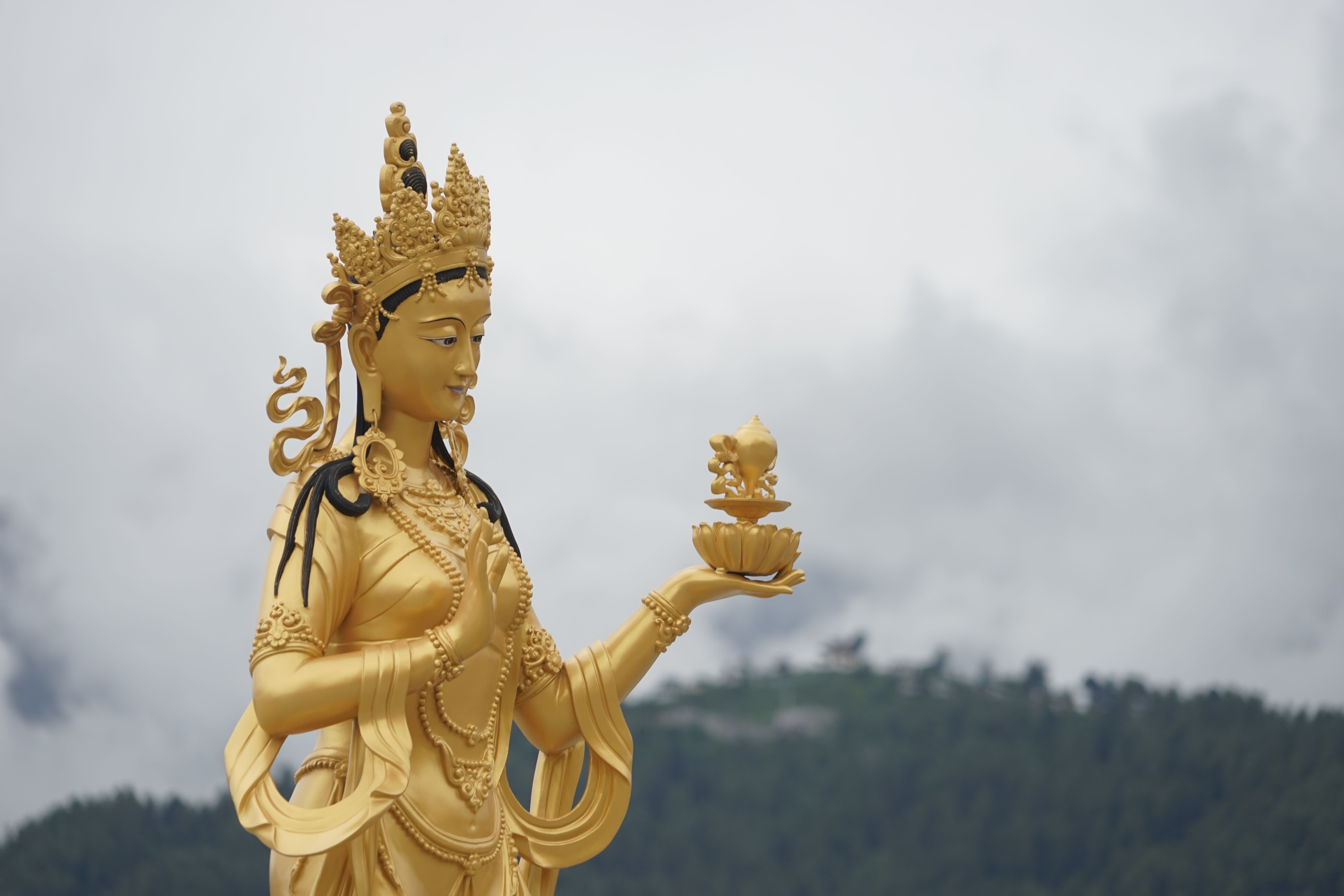 Golden Chenrezig bodhisattva statue against misty mountains, Thimphu Bhutan