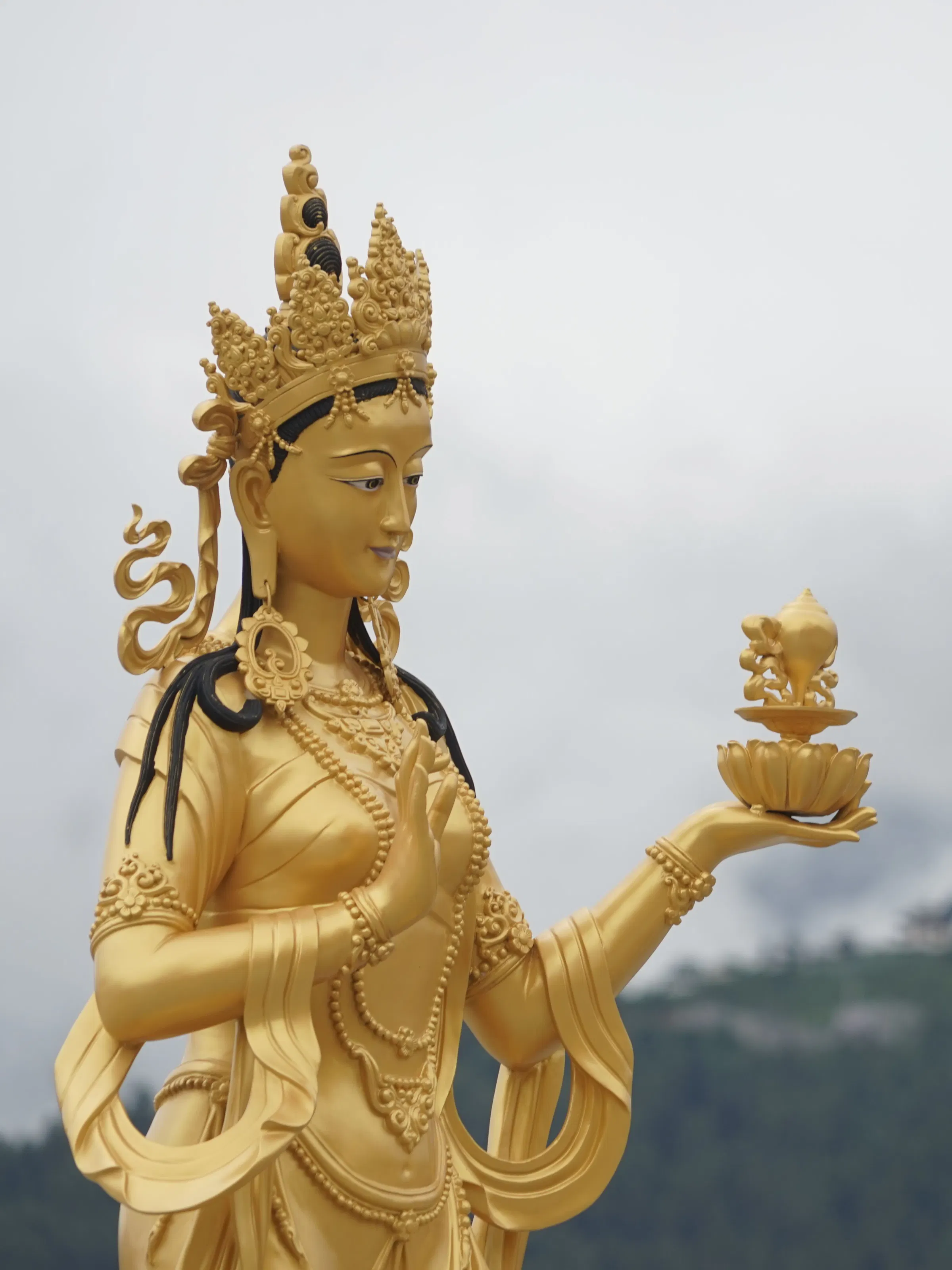 Golden Chenrezig bodhisattva statue against misty mountains, Thimphu Bhutan