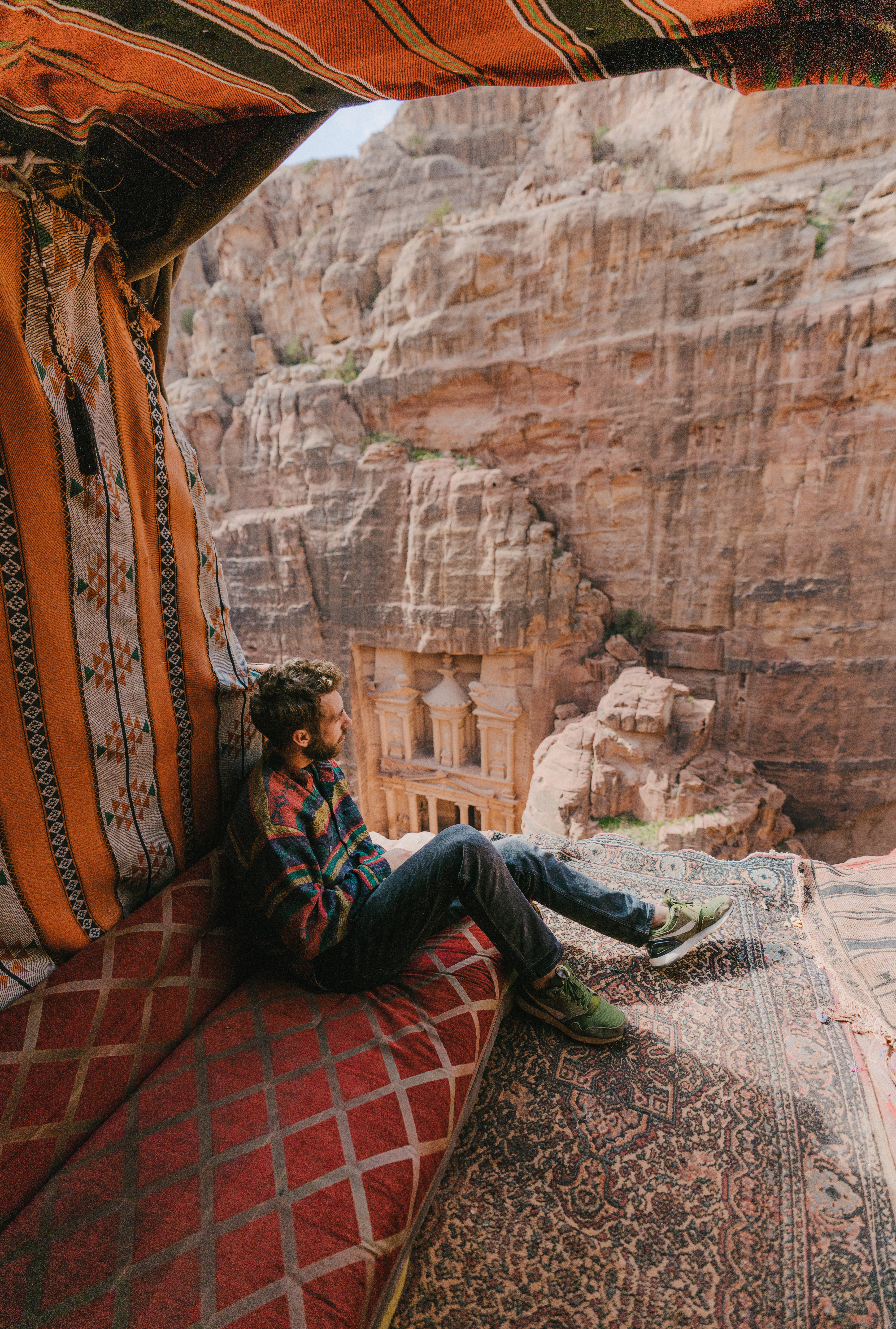 Person sitting on patterned cushions in a rock alcove overlooking a canyon.