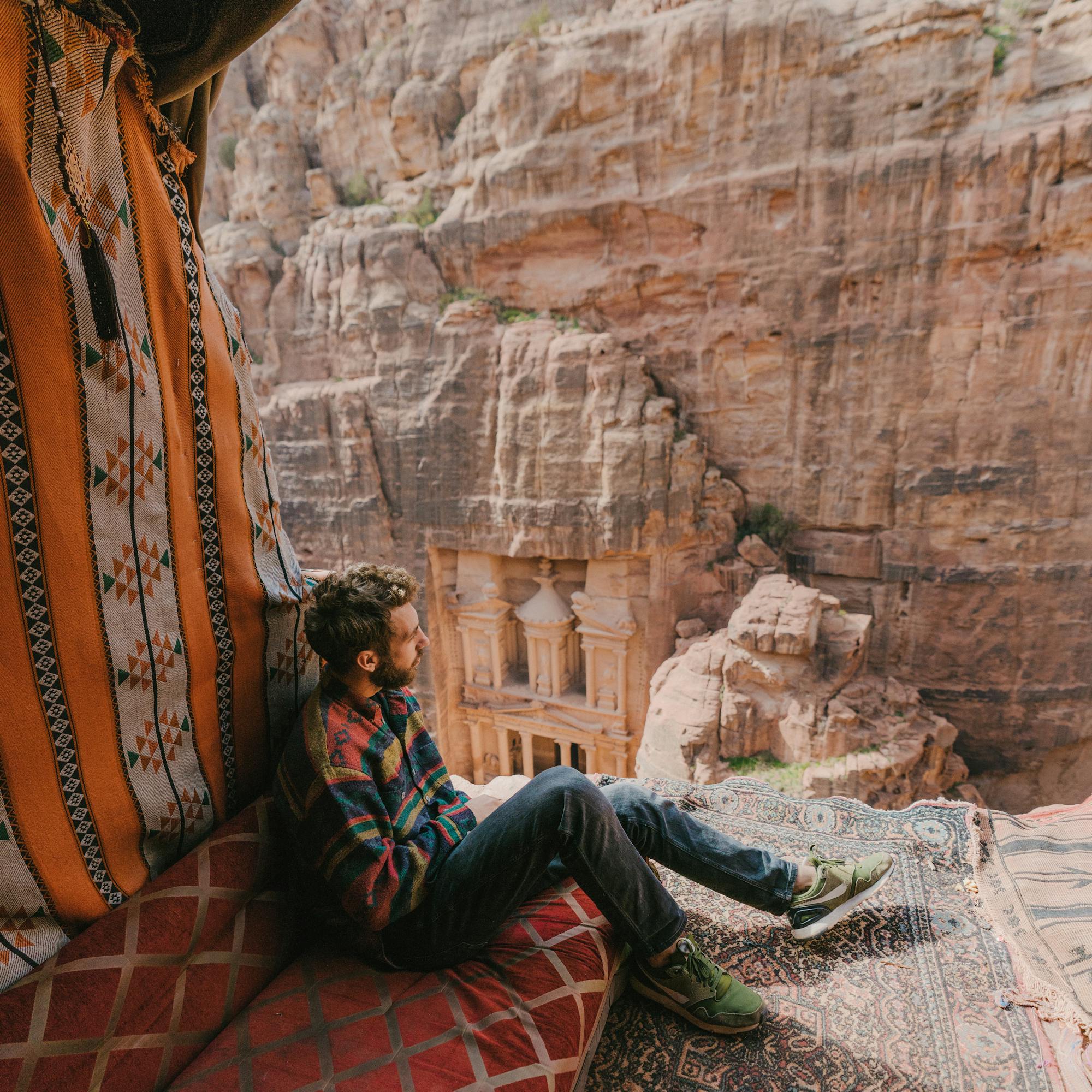 Person sitting on patterned cushions in a rock alcove overlooking a canyon.