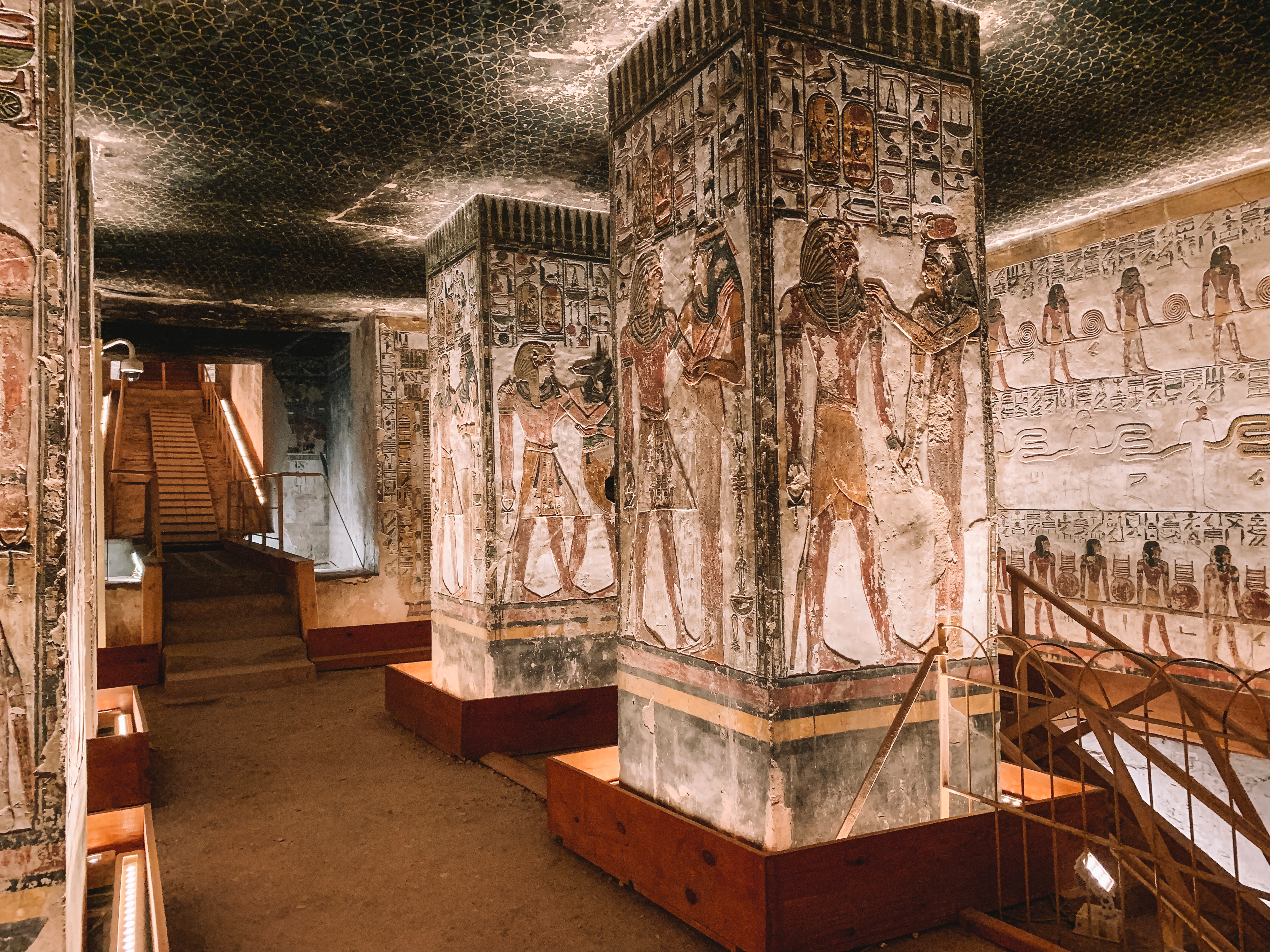 Painted pillars and walls line an ancient stone corridor lit by warm ceiling lights.