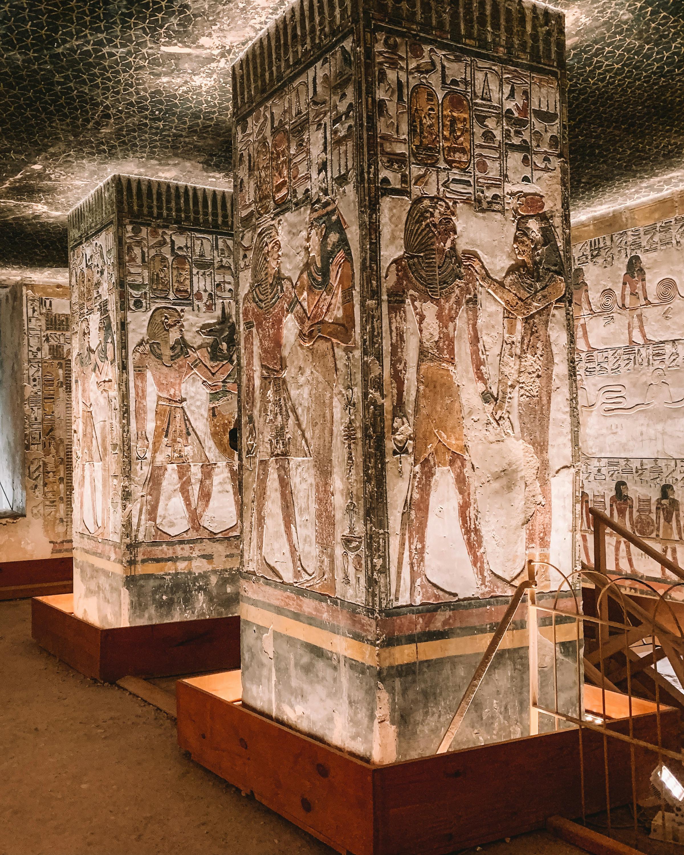 Painted pillars and walls line an ancient stone corridor lit by warm ceiling lights.