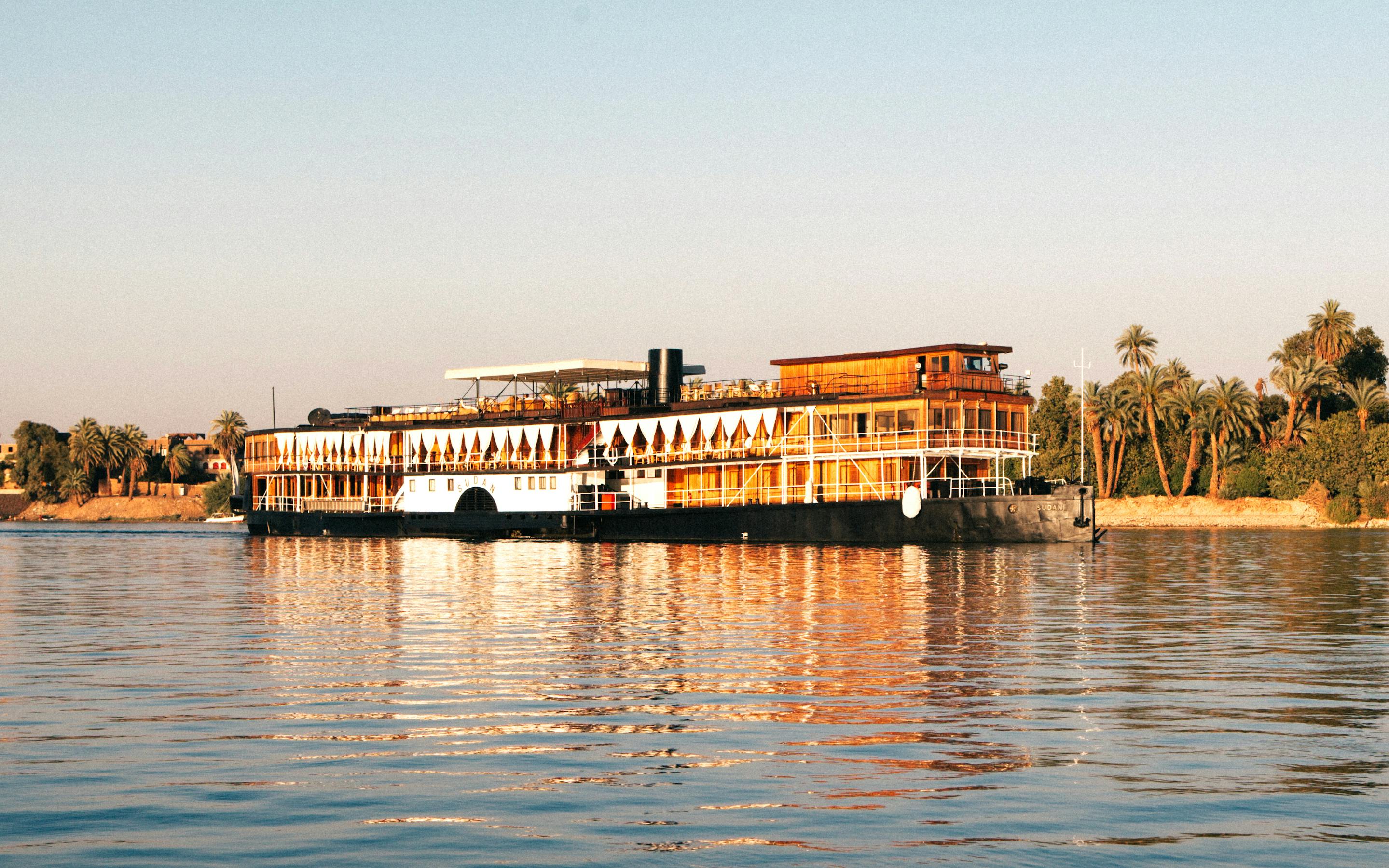 Large riverboat on calm water with a green shoreline and clear sky.