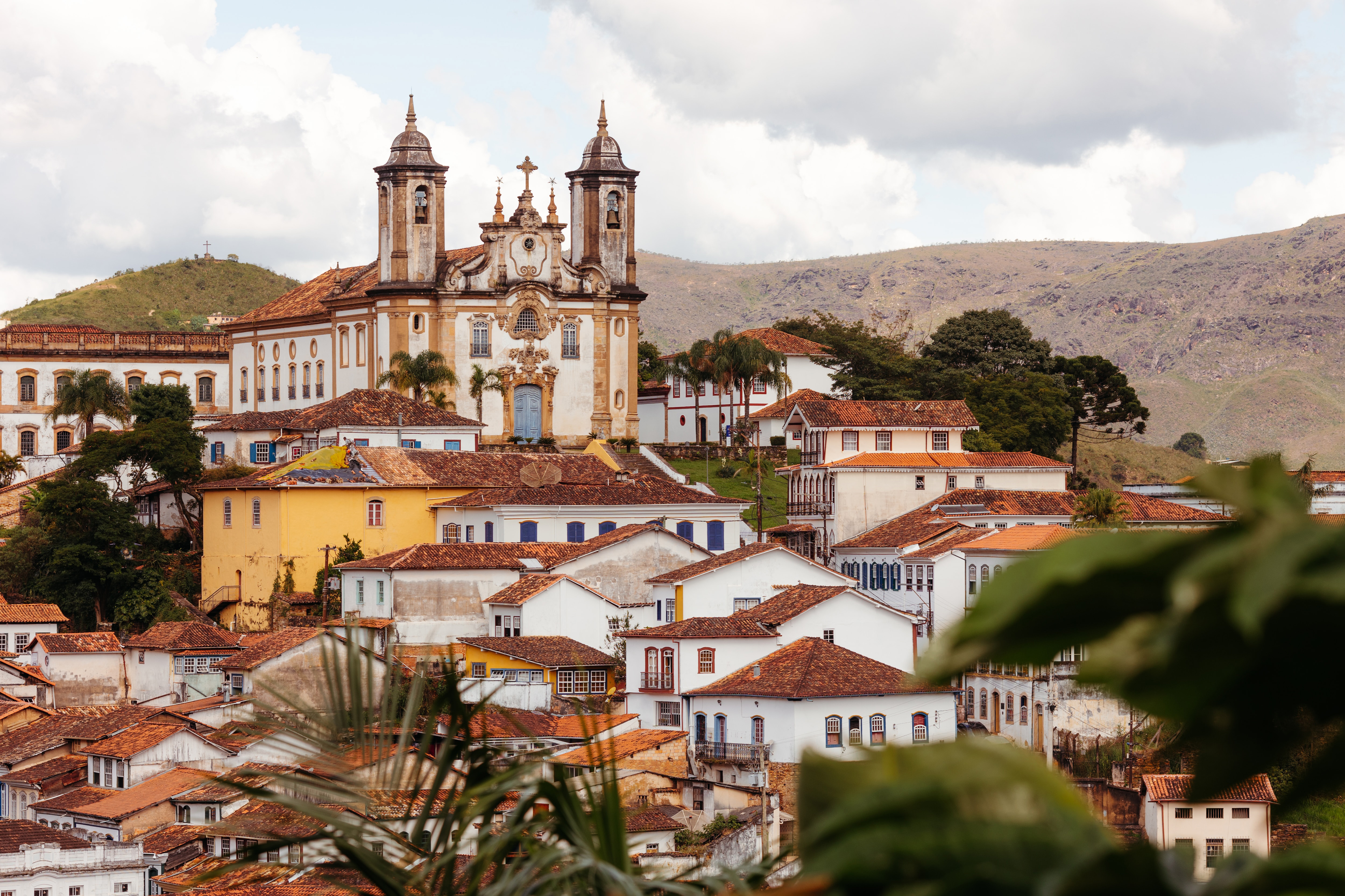 Colonial town spreads across a hillside, with twin church towers and colorful rooftops under a bright, cloudy sky in day light.
