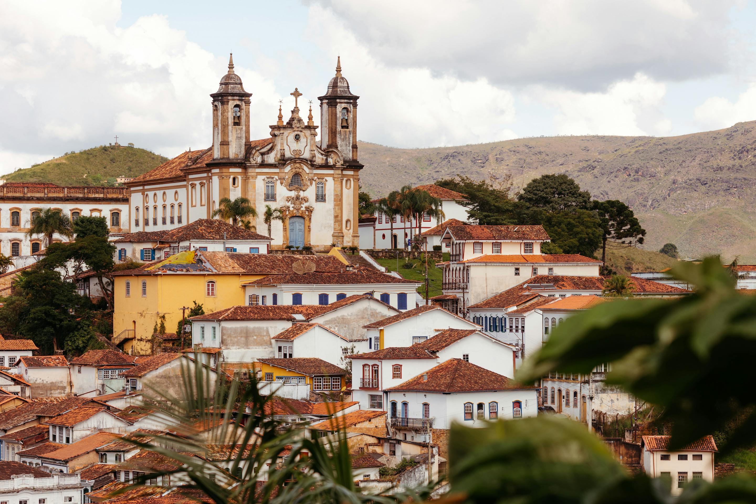Colonial town spreads across a hillside, with twin church towers and colorful rooftops under a bright, cloudy sky in day light.