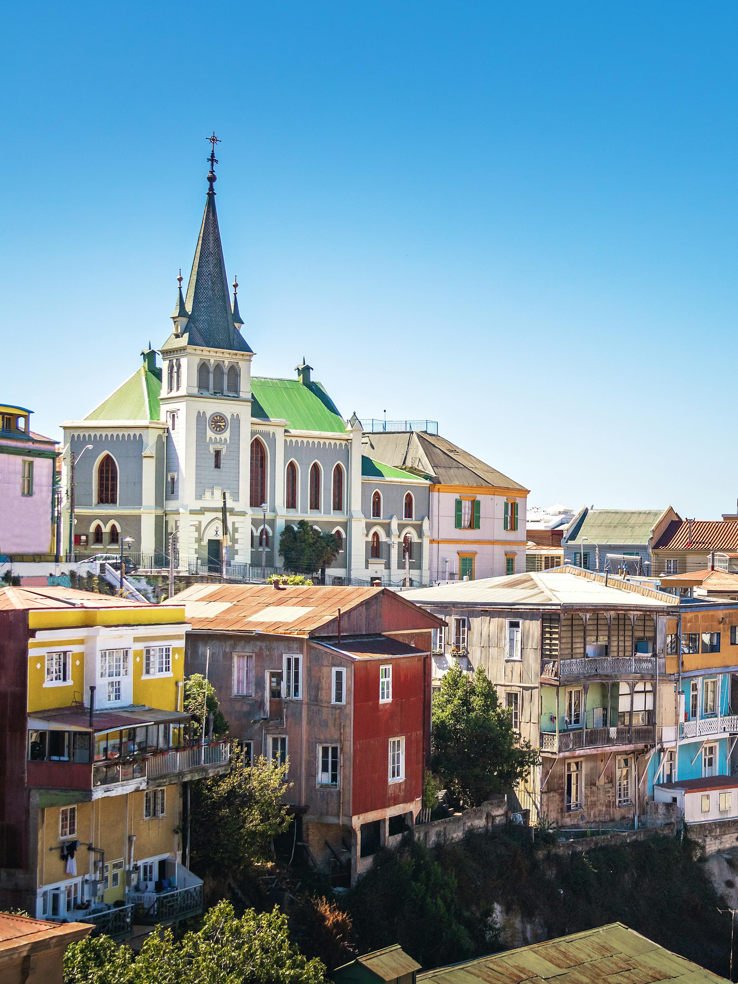 Colorful houses climb a steep hillside above the harbor, with a church spire and blue sky in view beyond them.